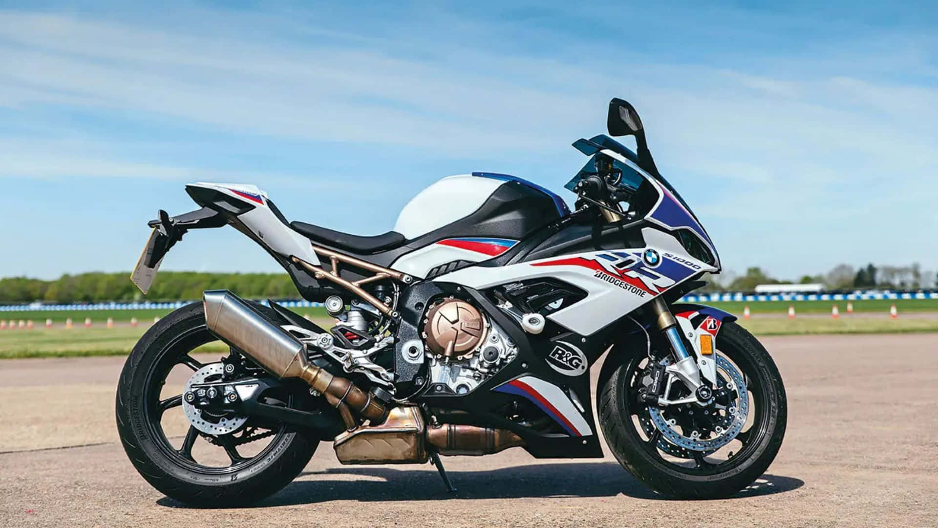 高性能量產 BMW S1000RR 賽車 壁紙 — 一架時尚的白、藍、紅 BMW S1000RR 電單車停泊在賽車場上，天空清澈湛藍。