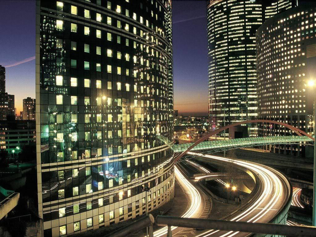 高聳的玻璃建築，亮著燈的窗戶和黃昏時發光的道路。
