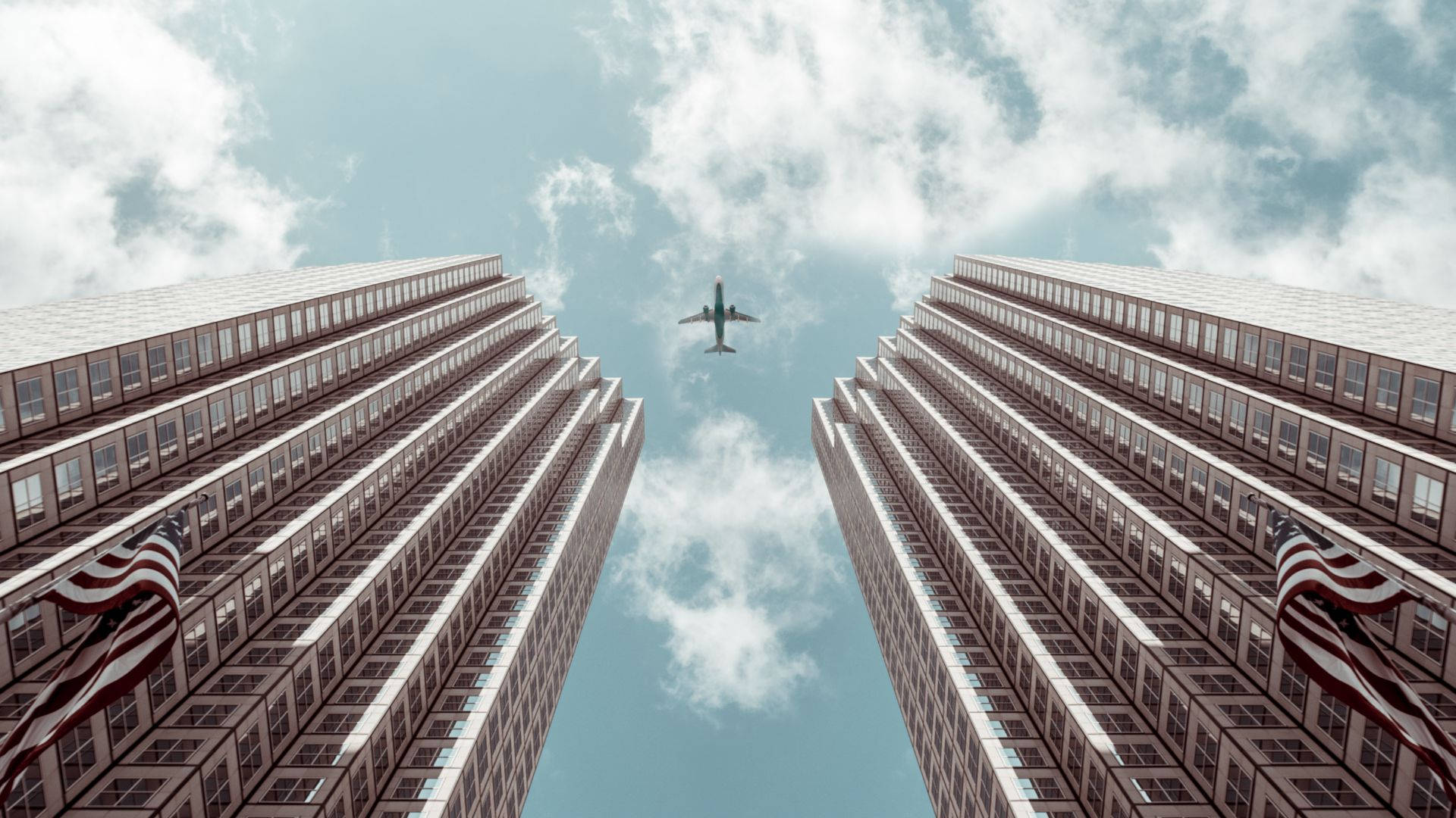 高樓間飛機視角 壁紙 — 低角度拍攝一架飛機在部分多雲的天空下，飛越兩座高聳摩天大樓之間。