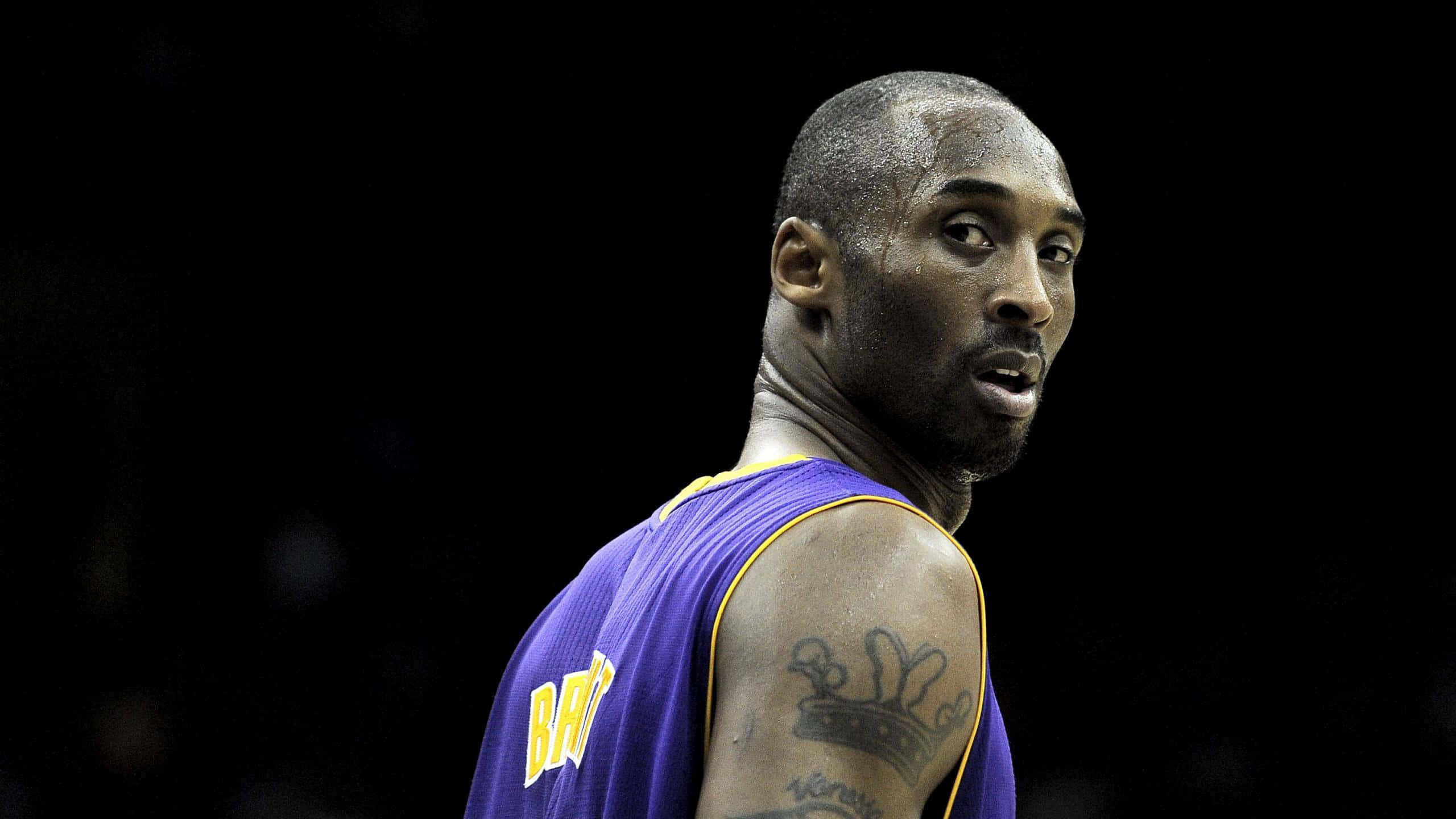 Kobe 桌布 壁紙 — 高比·拜仁身穿紫色湖人球衣，在深色背景下強烈凝視，肩上可見皇冠紋身。