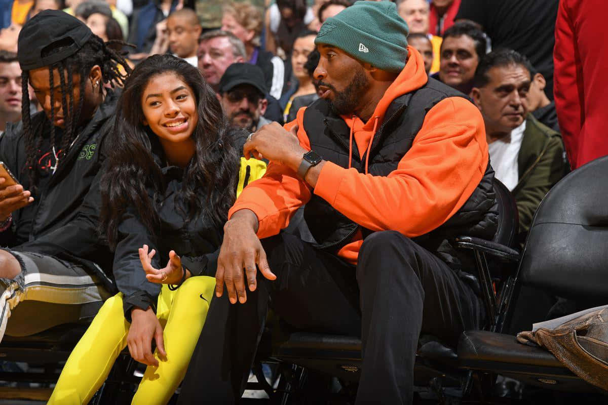 Kobe And Gigi 桌布 壁紙 — 高比拜仁和吉安娜拜仁坐在籃球場邊，被球迷包圍，微笑聊天。