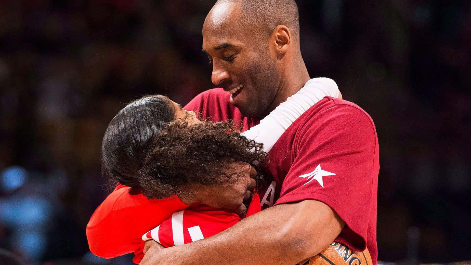Kobe And Gigi 桌布 壁紙 — 高比拜仁在籃球活動中，以溫暖的笑容擁抱一位身穿紅色球衣的小女孩。