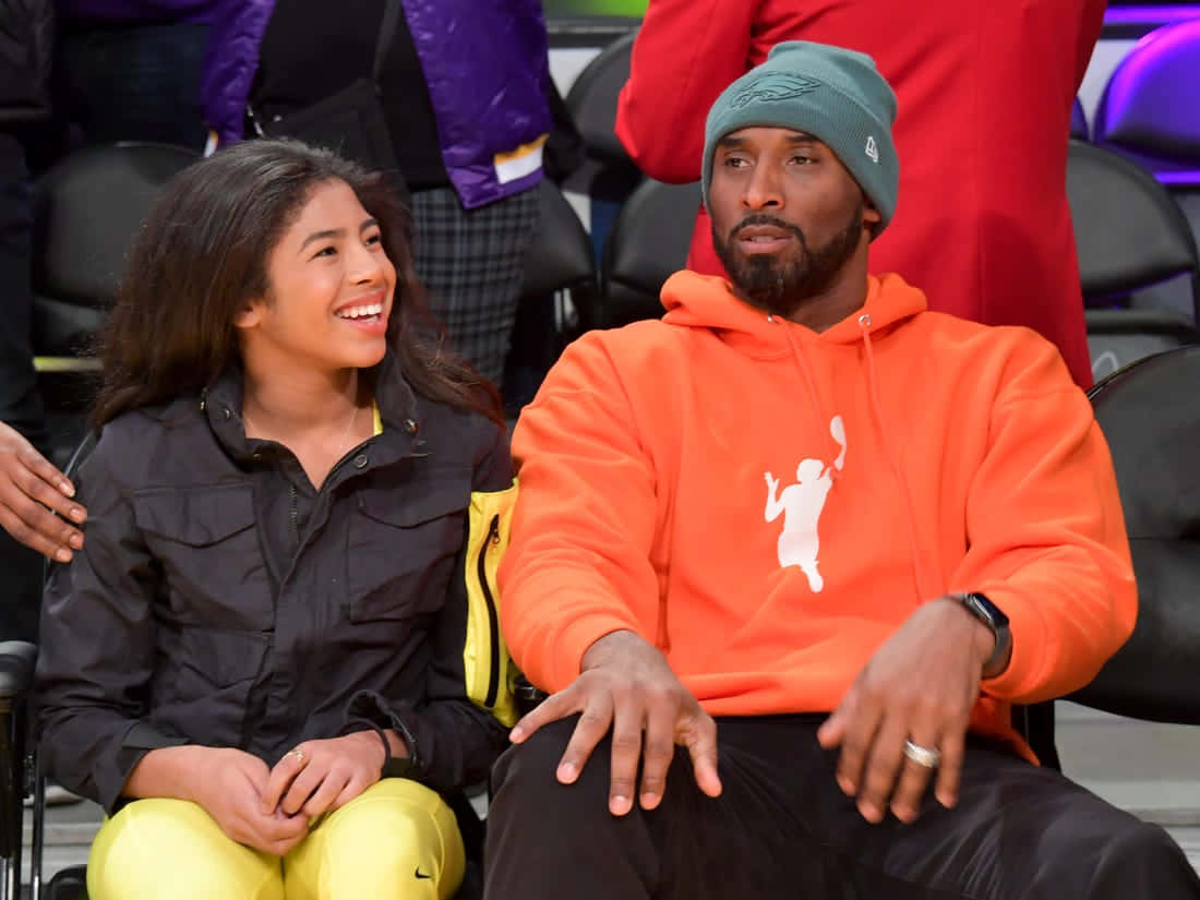 Kobe And Gigi 桌布 壁紙 — 高比拜仁與女兒吉安娜在籃球比賽中穿著鮮豔的橙色和黃色服裝一起微笑。