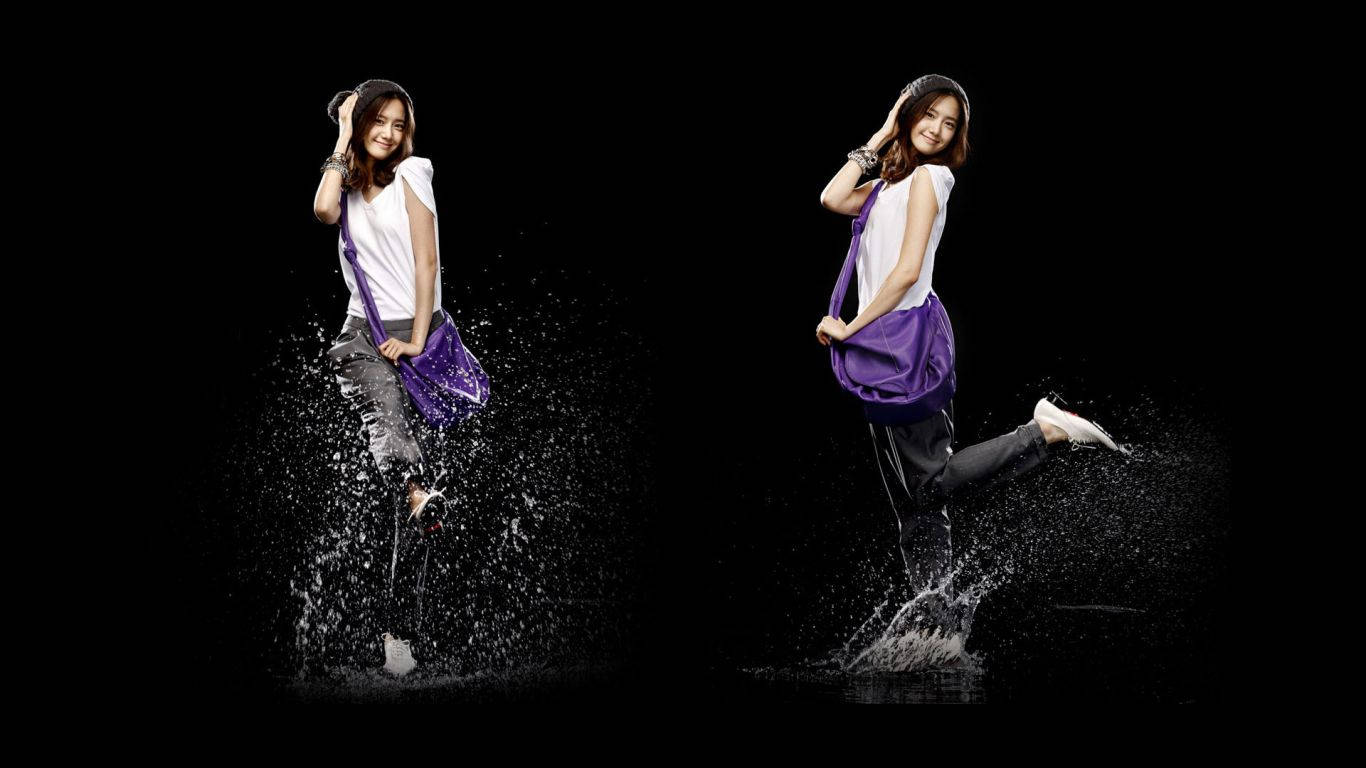 高清 Yoona 雨滴特效畫面 壁紙 — 一名身穿白襯衫和牛仔褲的女子在黑色背景前歡快地跳過水花。