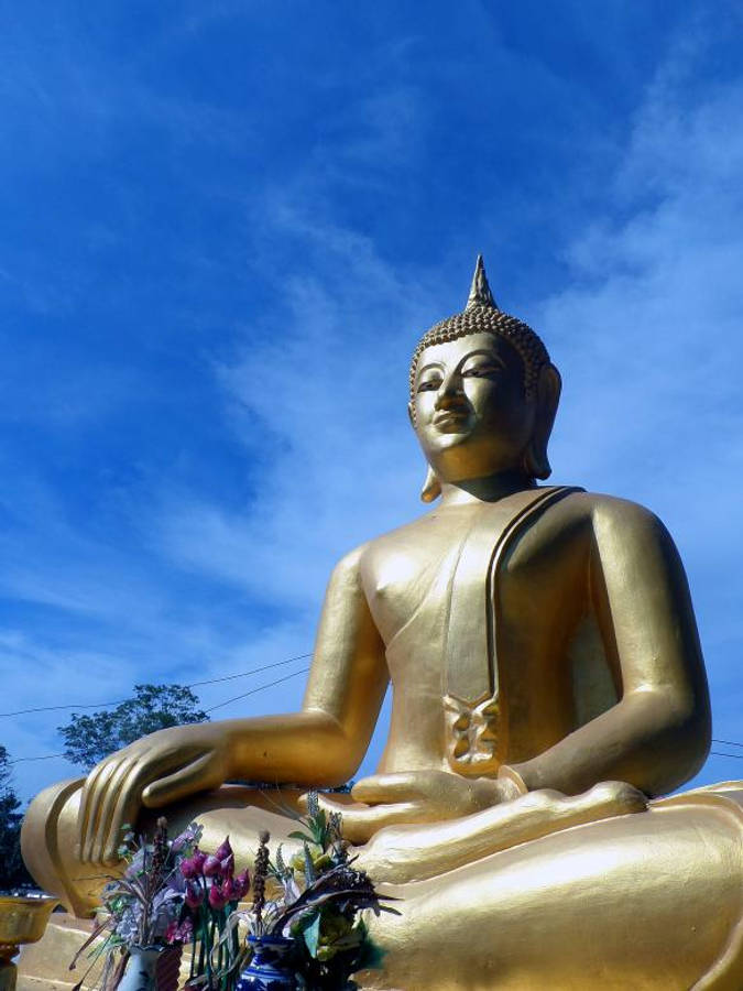 高清佛像，寧靜祥和 壁紙 — 一座高聳的金色佛像在藍天白雲下寧靜地坐著。