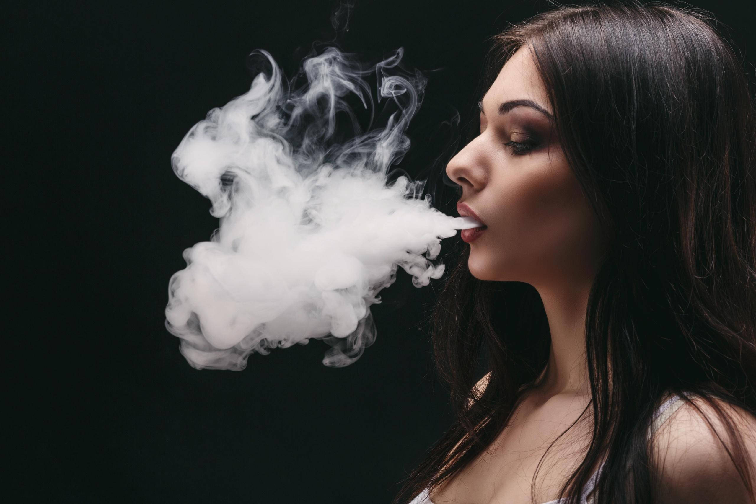 高清女孩 吸煙霧 壁紙 — 一位深色頭髮的女性在純黑背景上呼出一團濃厚的蒸氣雲。