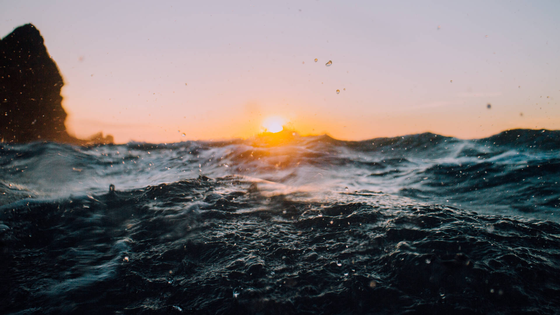 夕陽映照海洋，波浪飛濺，懸崖為背景