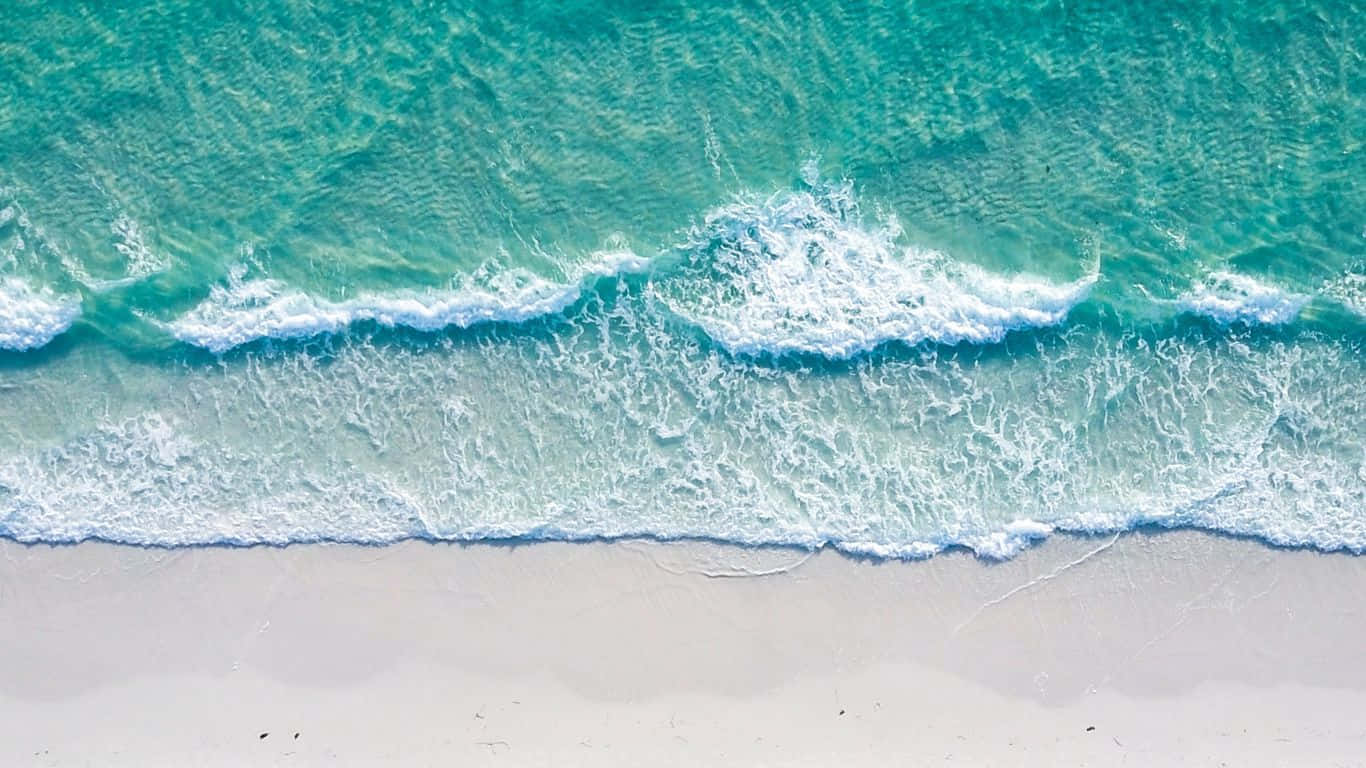 碧綠色的海浪輕輕湧上白色沙灘的俯瞰圖。