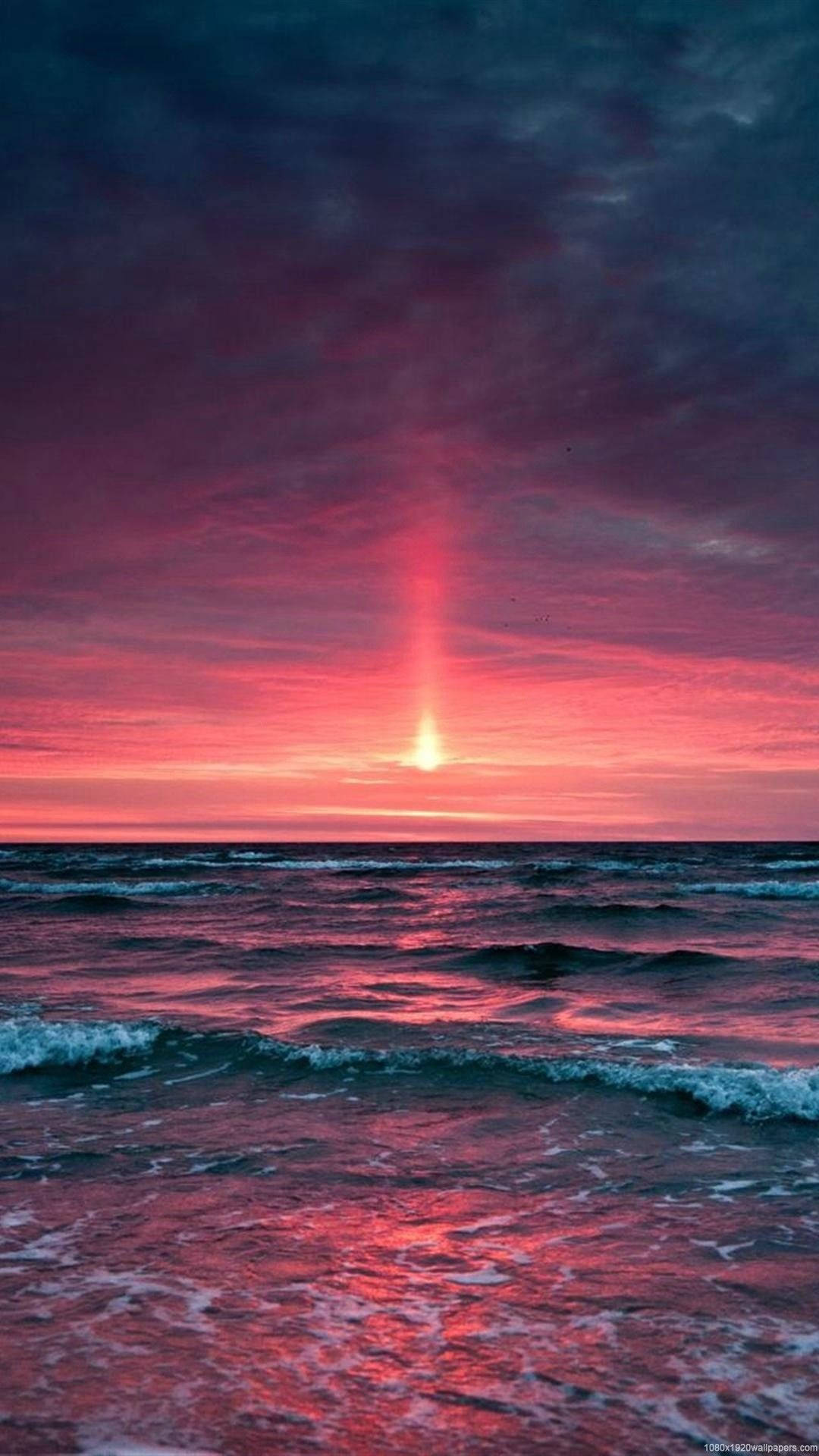 海洋上空鮮豔的日落，紅色和紫色的天空倒映在水面上。