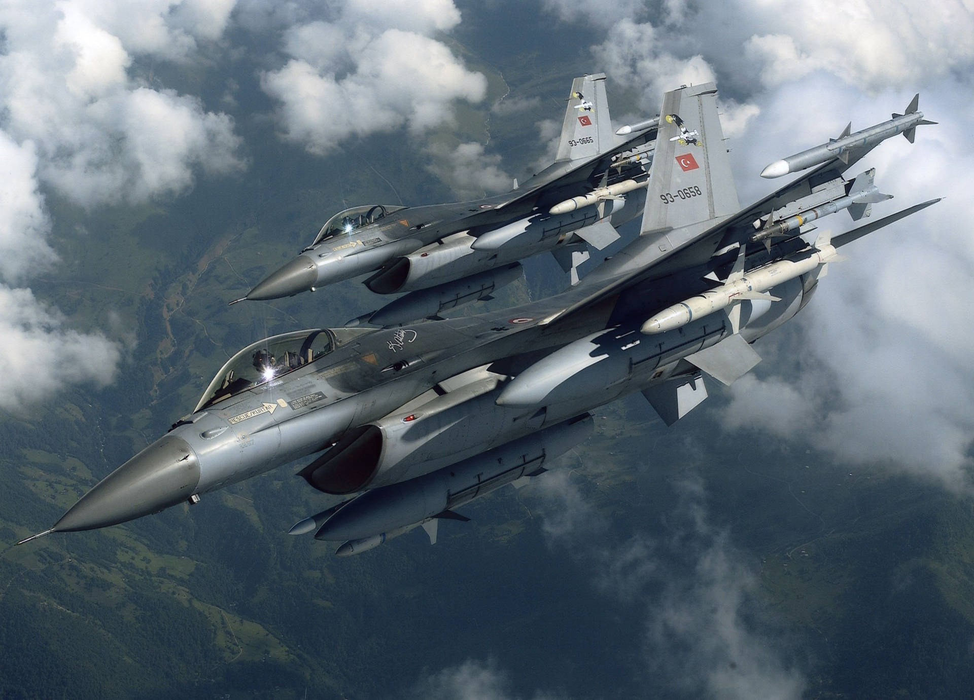 兩架戰機在山脈和雲層上空編隊飛行。