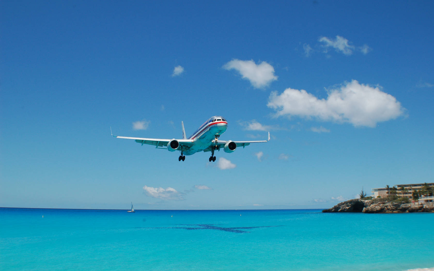 飛機在晴朗藍天下於海灘附近的碧綠色海洋上空降落