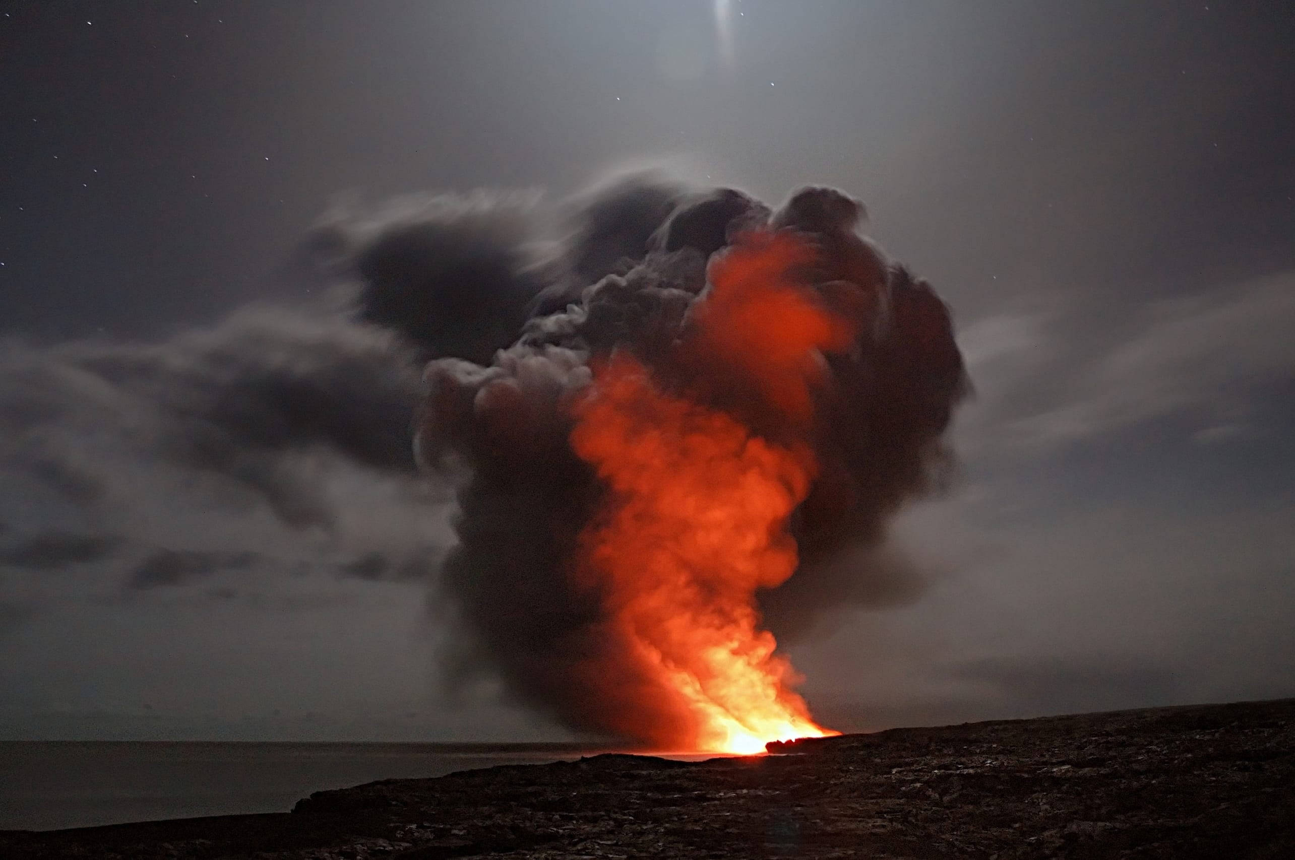 高溫火焰與灰燼煙霧 壁紙 — 夜晚火山爆發，在黑暗的海洋地平線之上，向星空噴射出熾熱的橙色熔岩和煙霧柱。