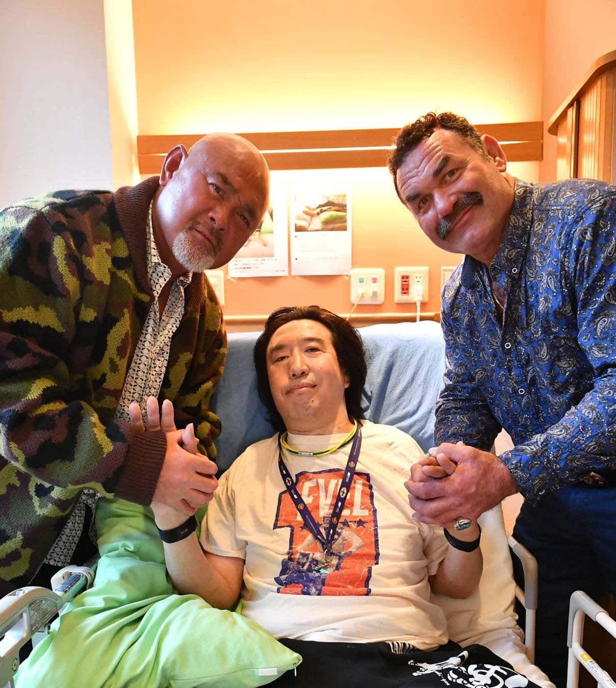 三名男子在醫院病房支持一名坐輪椅的男子。