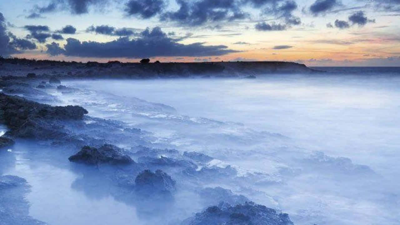 高畫質 720p 寬螢幕背景 壁紙 — 薄霧籠罩的海浪在暮色中輕輕拍打著深色火山岩，天空多雲。