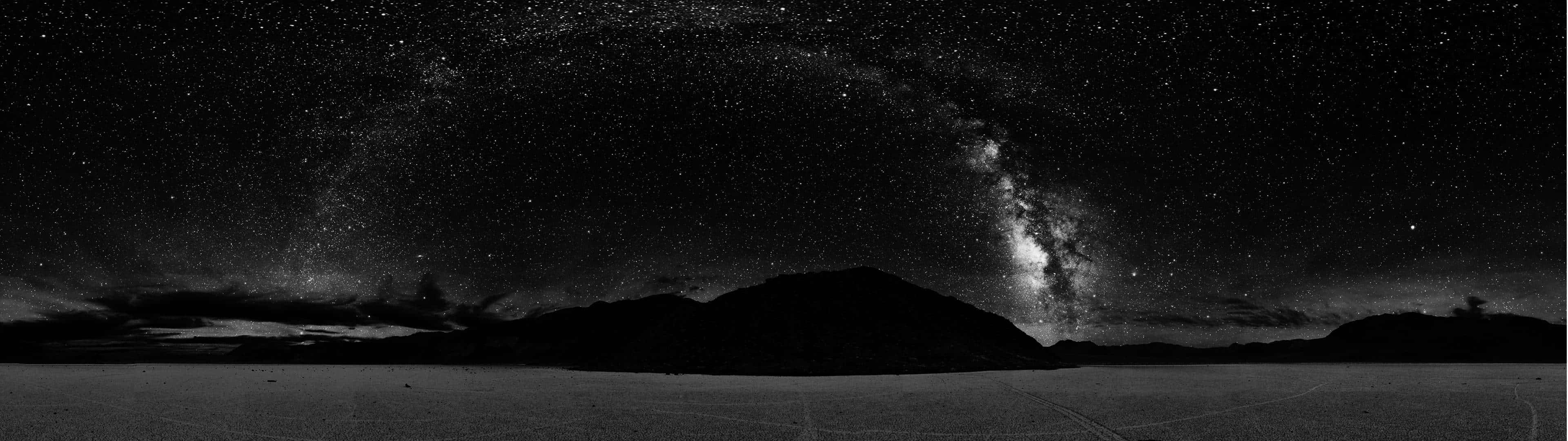 高畫質呈現的浩瀚宇宙 壁紙 — 在繁星點點的夜空下，銀河橫跨在剪影般的山脈之上，令人嘆為觀止的黑白全景。