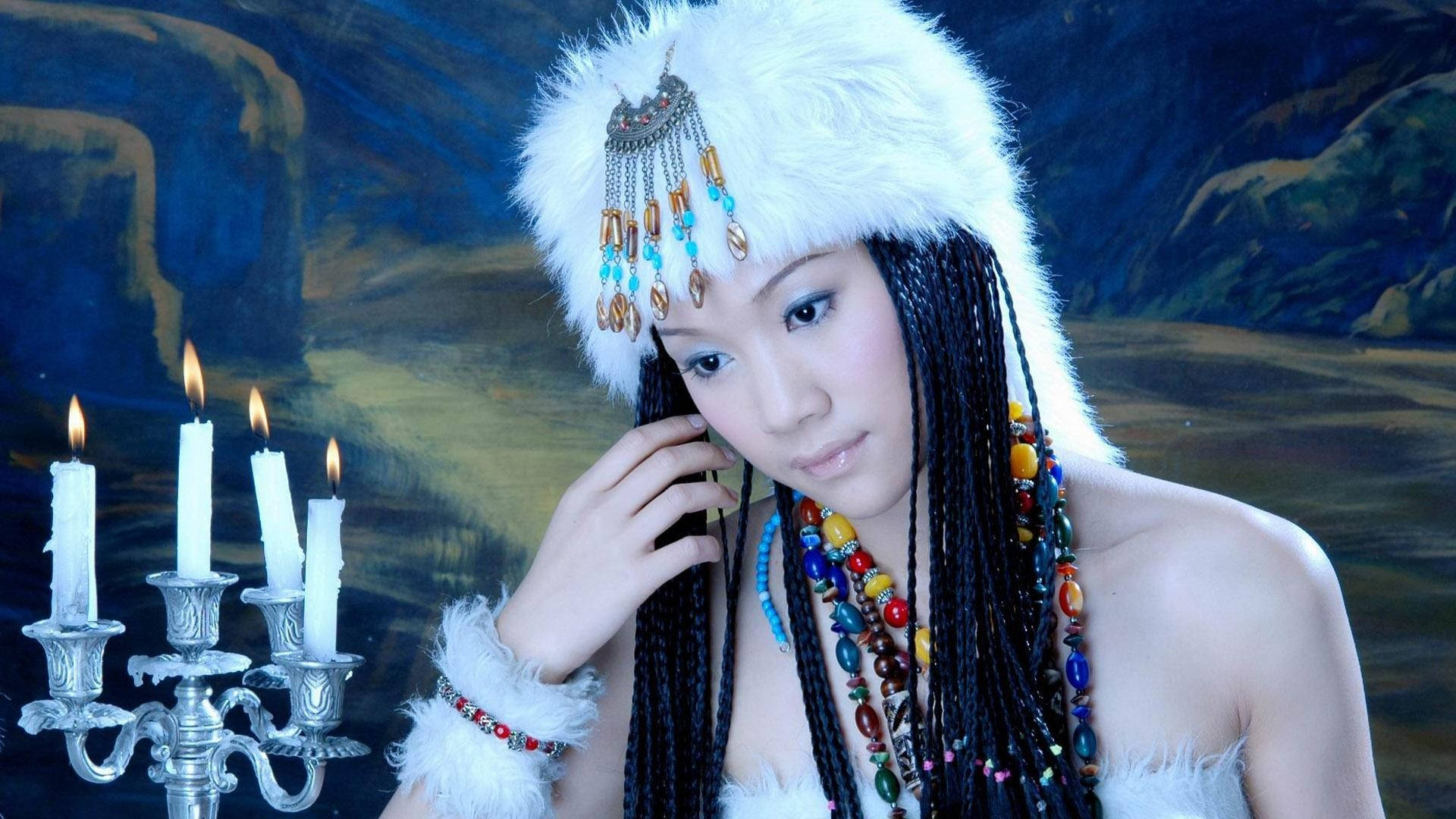戴著傳統毛帽和珠子首飾的女人，站在點燃的燭台旁。