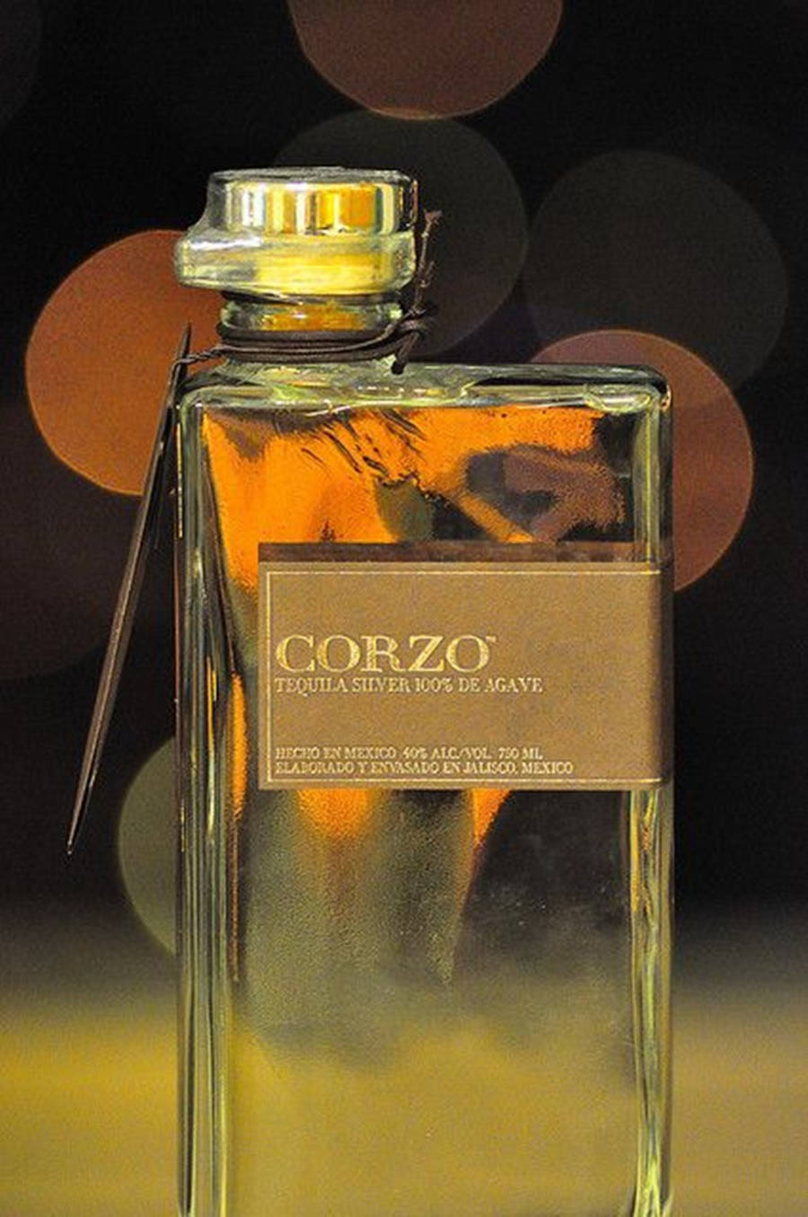 一瓶帶有金色液體和散景背景的 Corzo Silver Tequila。