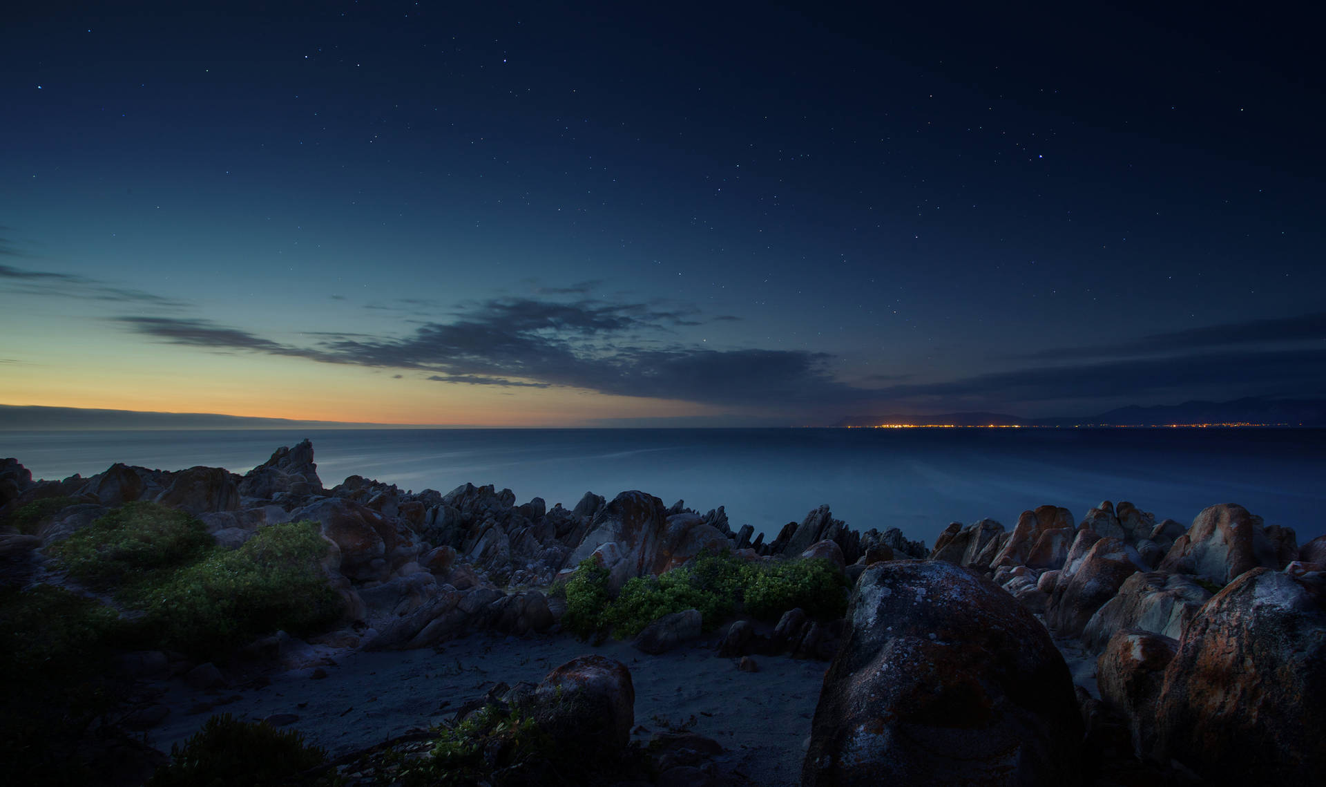 夜晚的岩石海岸，星空下遠方的城市燈光。