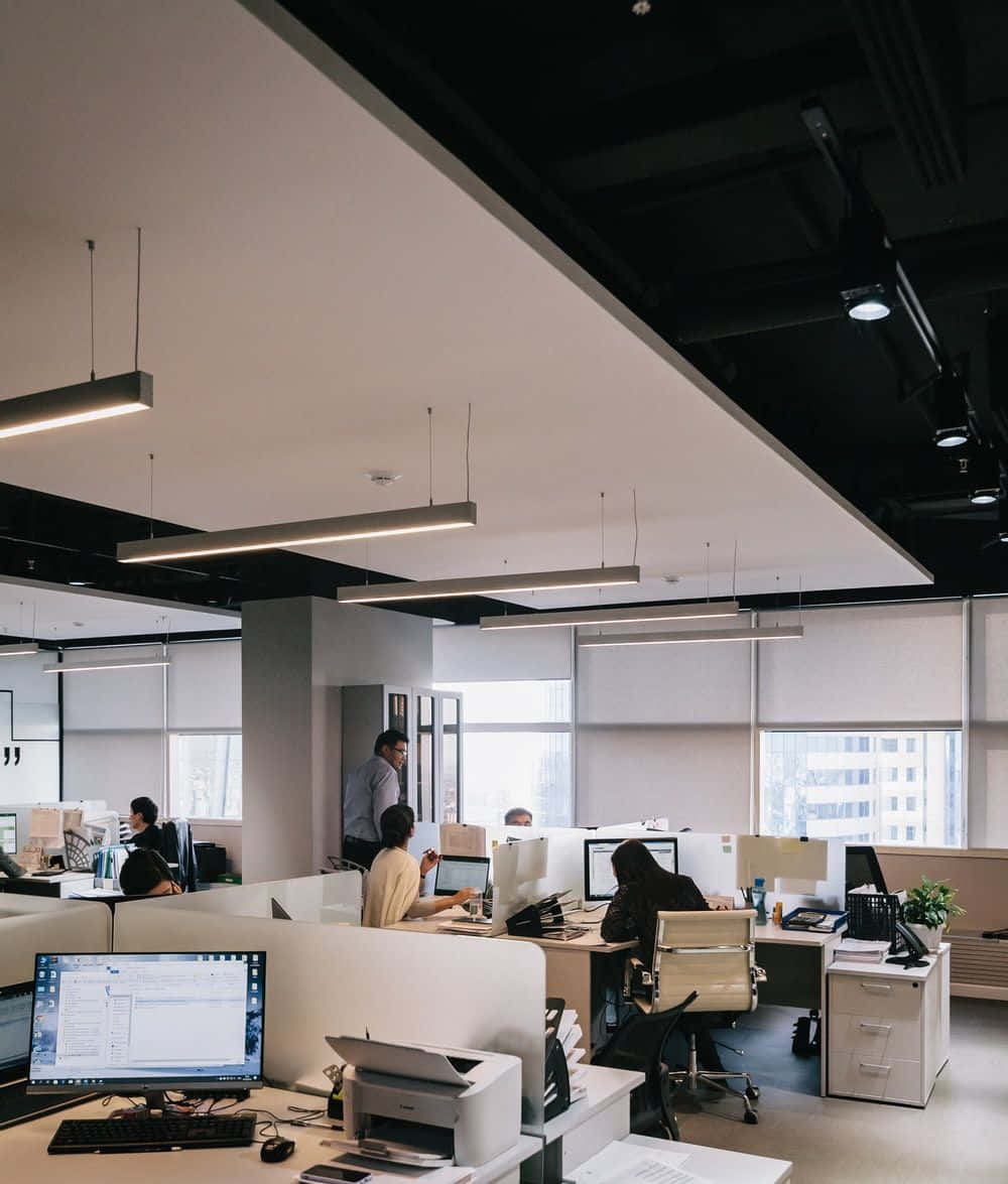在明亮現代辦公室中，員工在電腦工作站工作，天花板燈具外露。