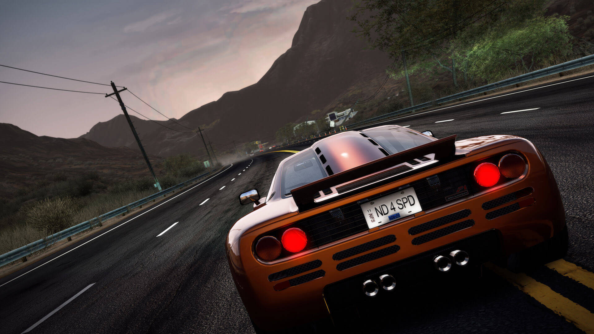 高畫質麥拉倫F1跑車 壁紙 — 一輛青銅色的McLaren F1在黃昏時分沿沙漠高速公路飛馳，背景是連綿的山脈。