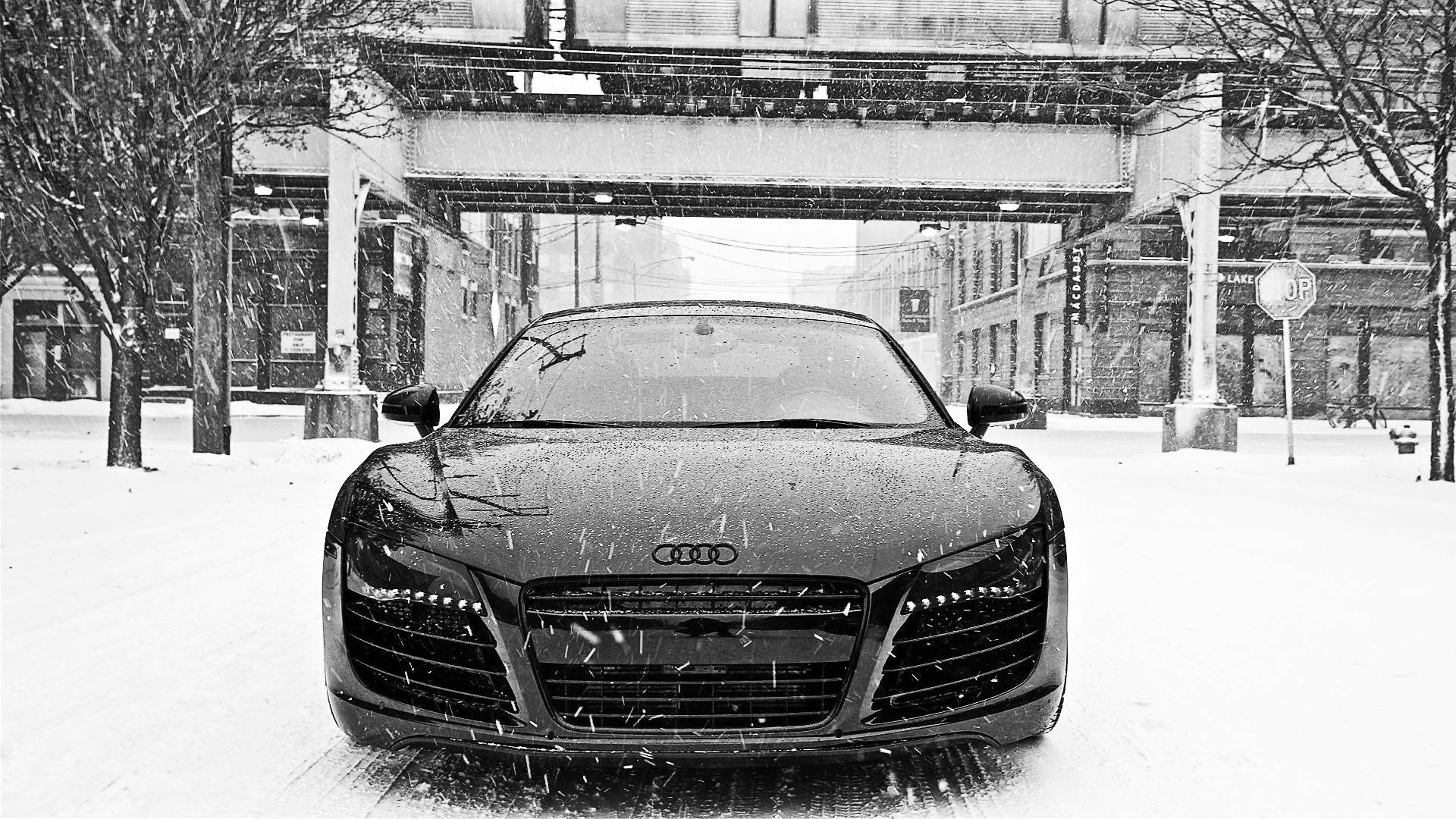 高畫質黑色奧迪R8跑車 壁紙 — 一架時尚的黑色奧迪R8停泊在積雪的城市街道上，天橋下雪花飄落。
