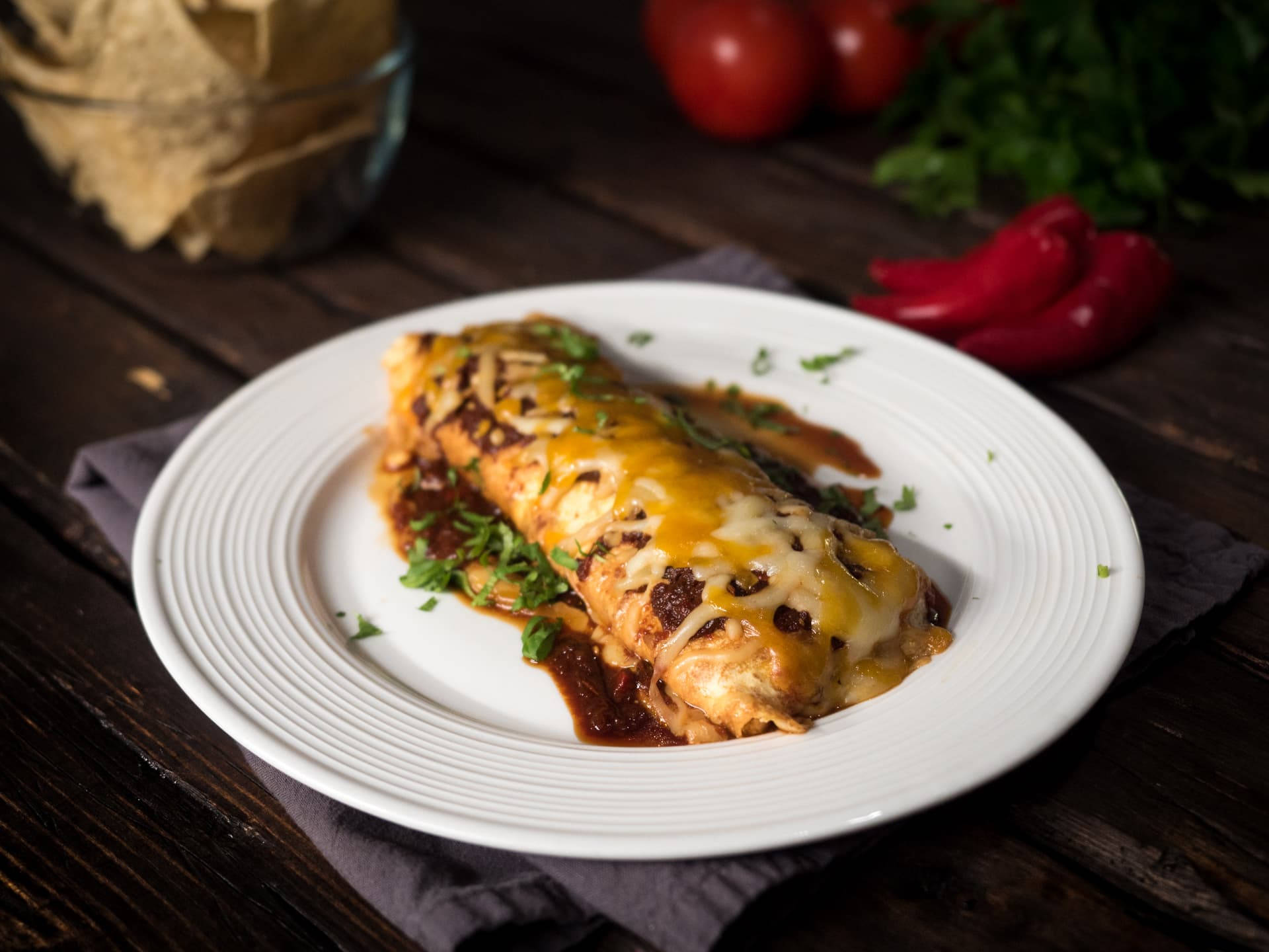 高級 enchiladas 盤中盛放 壁紙 — 一個鋪滿醬汁並以芫荽裝飾的芝士墨西哥捲餅，放在深色木桌上的一個白色碟子上。