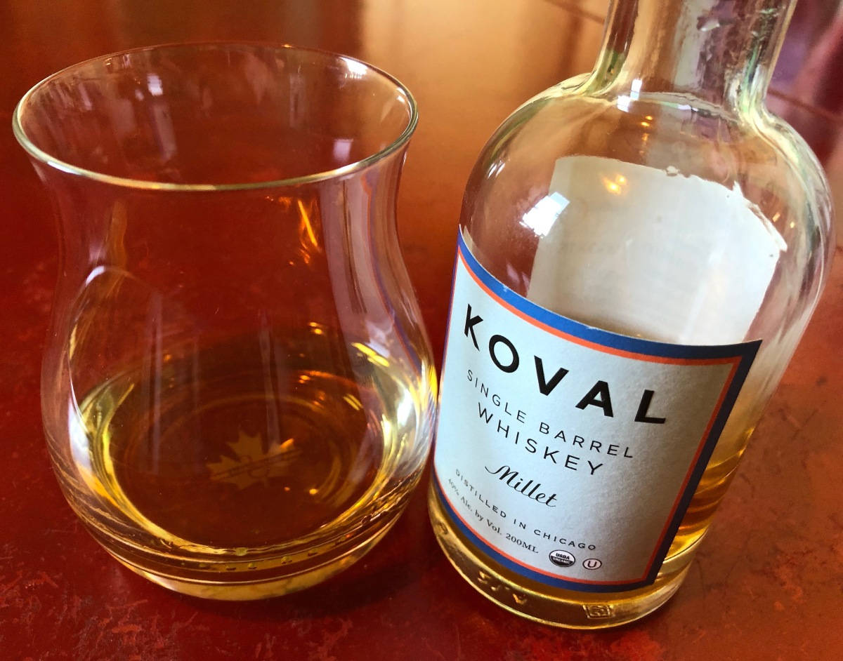一瓶 Koval Millet 威士忌放在紅色木桌上，旁邊有一個玻璃杯。