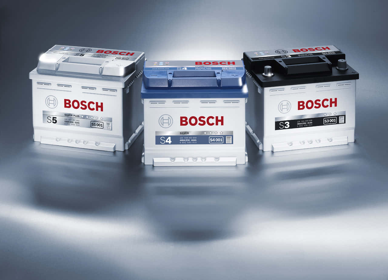 高級Bosch汽車電池 壁紙 — 三個銀藍色和黑色型號的博世汽車電池在工作室燈光下展示在反光金屬表面上。