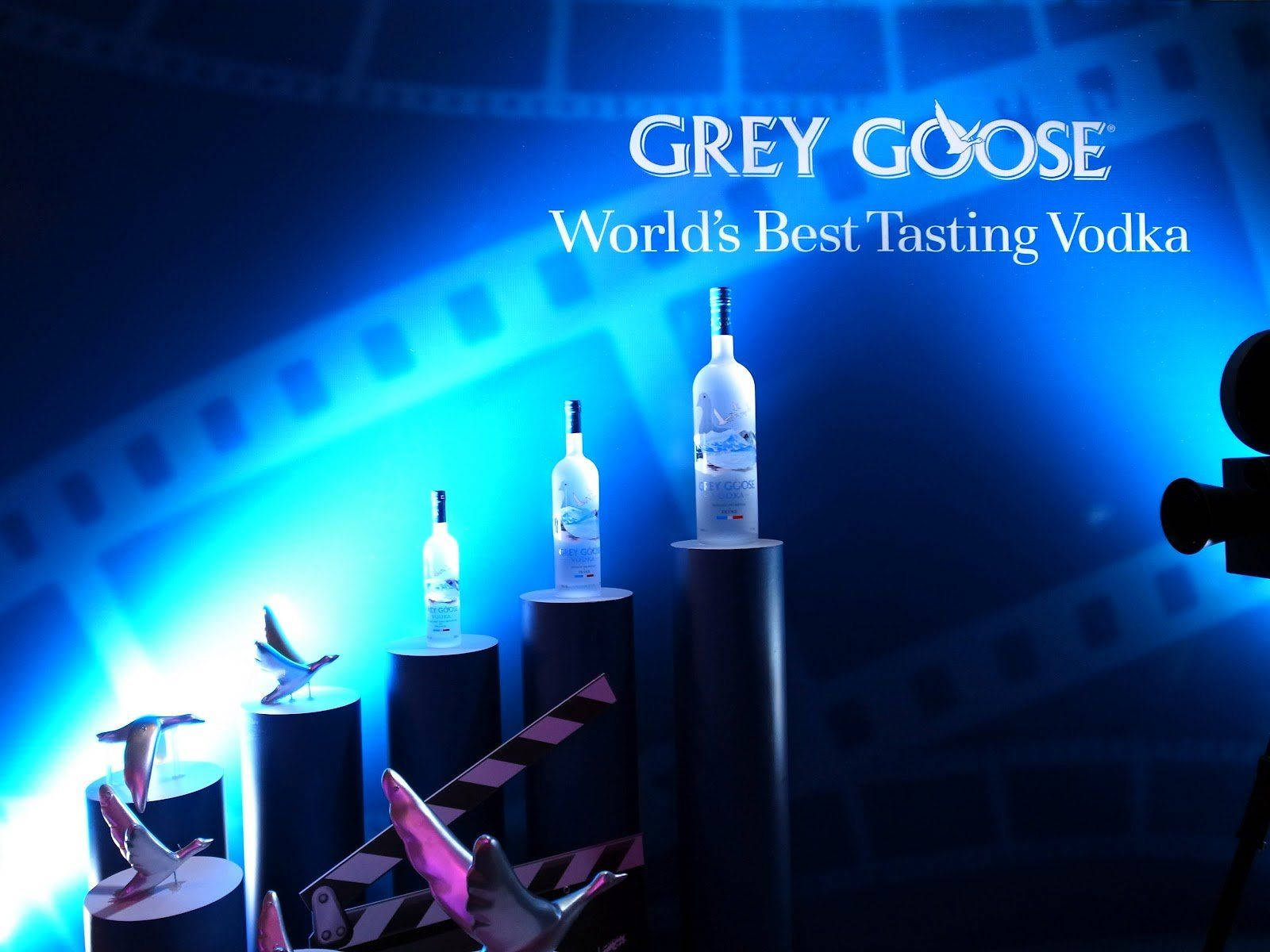 在藍色燈光的攝影棚中，Grey Goose 伏特加酒瓶置於底座上，配有膠片條和場記板。