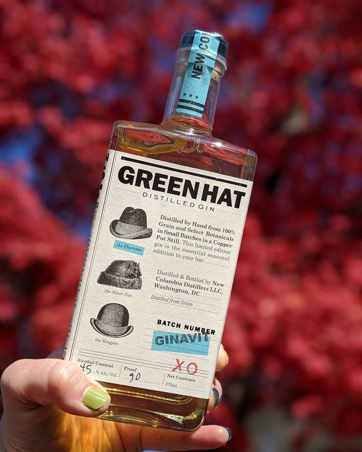 手拿著一瓶Green Hat氈酒，背景是紅色樹葉。