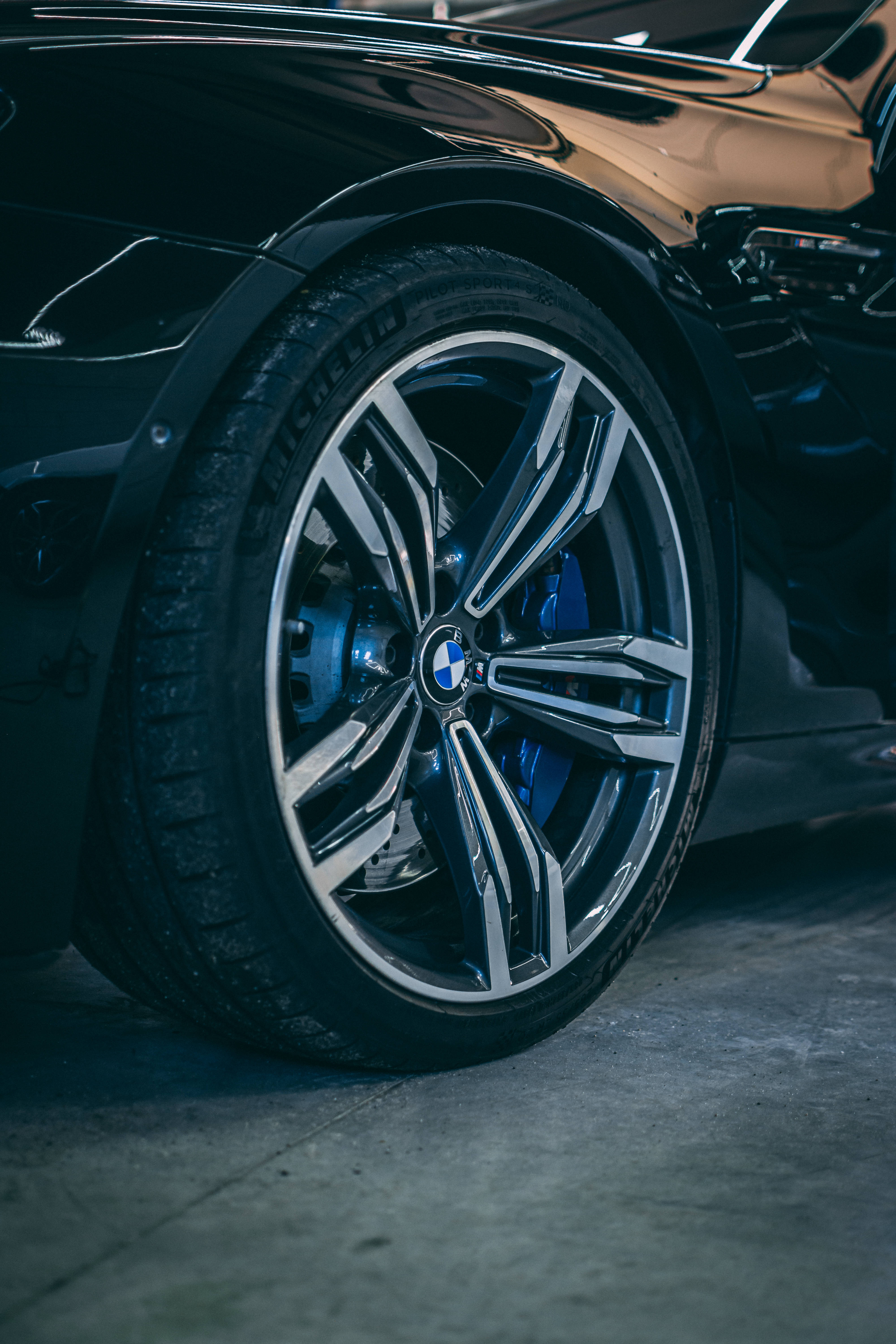 高級黑色BMW輪圈 壁紙 — 近距離拍攝一個時尚的黑色BMW汽車輪圈，配有藍色制動卡鉗和閃亮的鍍鉻輪輞，在戲劇性燈光下。