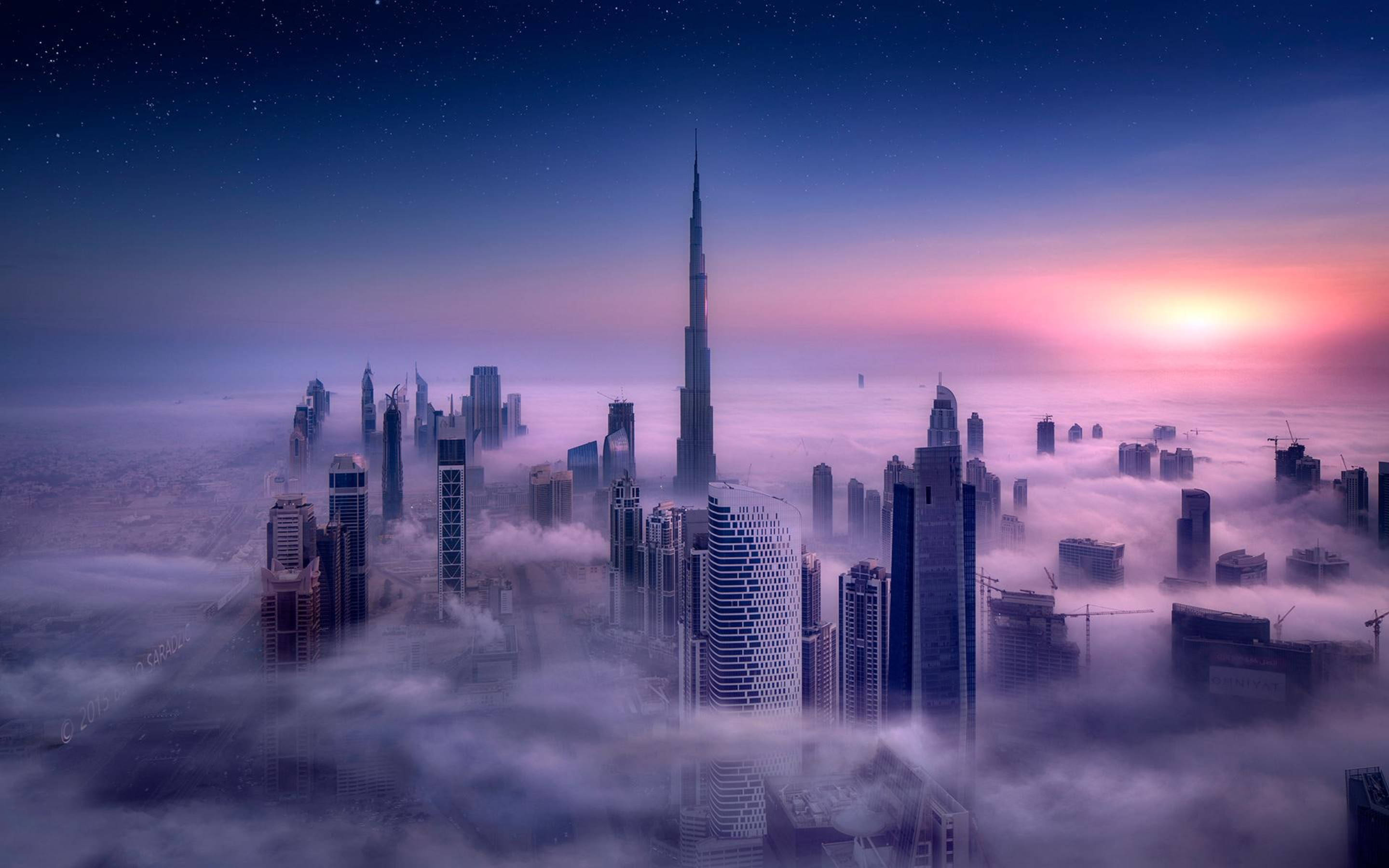  壁紙 — 高聳入雲的摩天大樓在黎明時分刺穿一片霧海，頭頂上星光漸逝，地平線上太陽閃耀。