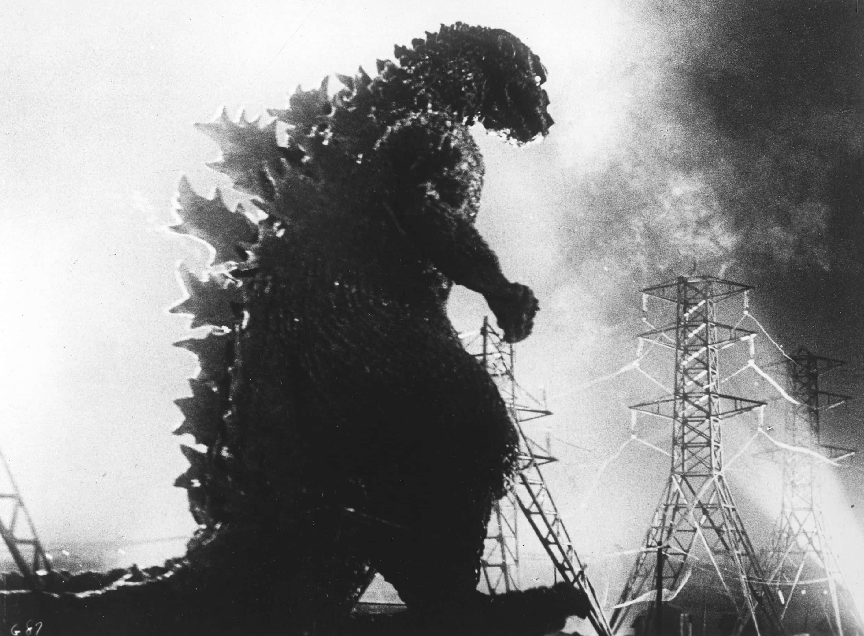 Godzilla 1954 桌布 壁紙 — 高聳的哥斯拉剪影穿過煙霧，旁邊是受損的電塔，構成戲劇性的黑白場景。