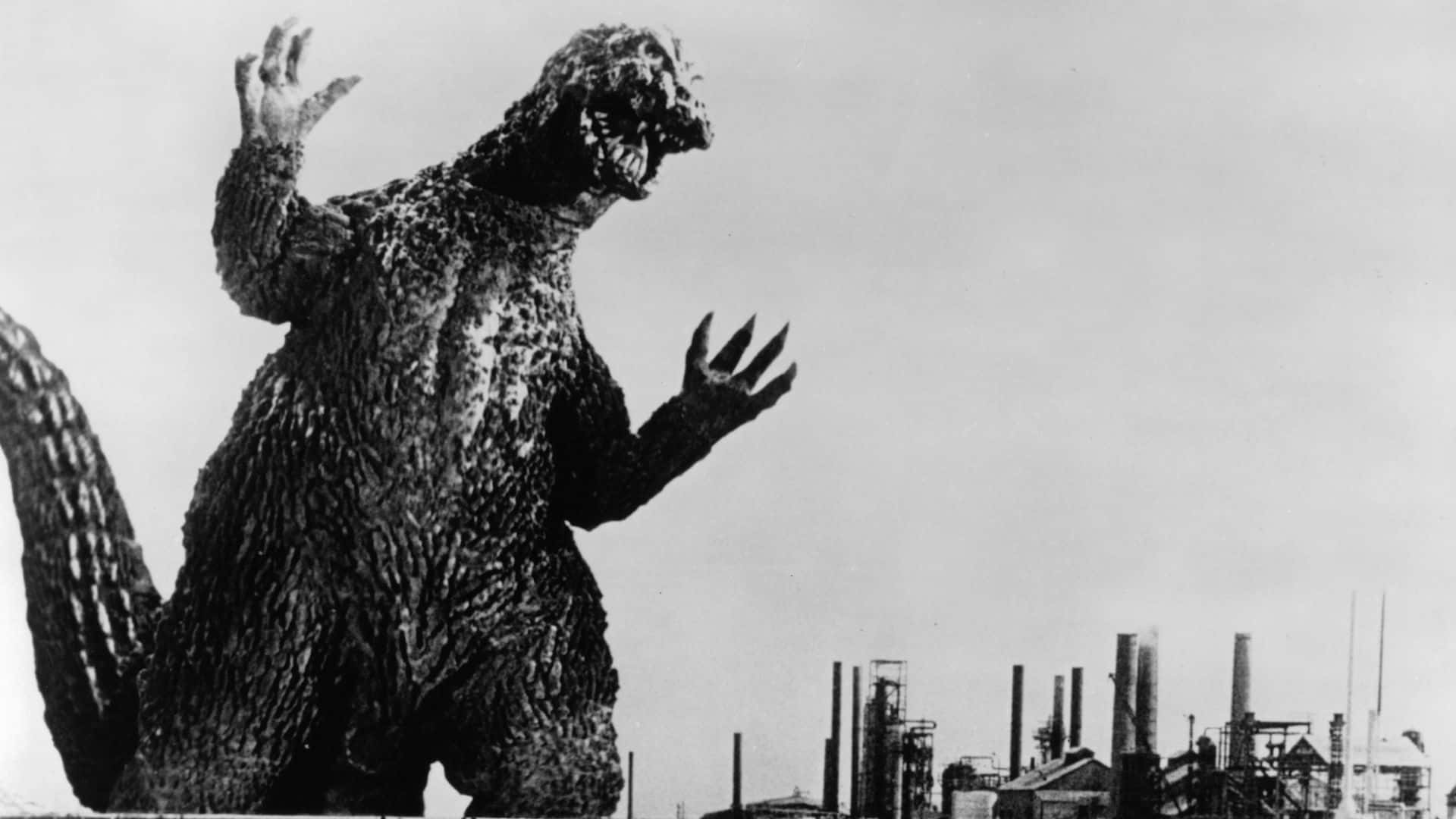 Classic Godzilla 桌布 壁紙 — 高聳的哥斯拉在戲劇性的黑白照片中，威嚇地站在有煙囪的工業城市景觀之上。