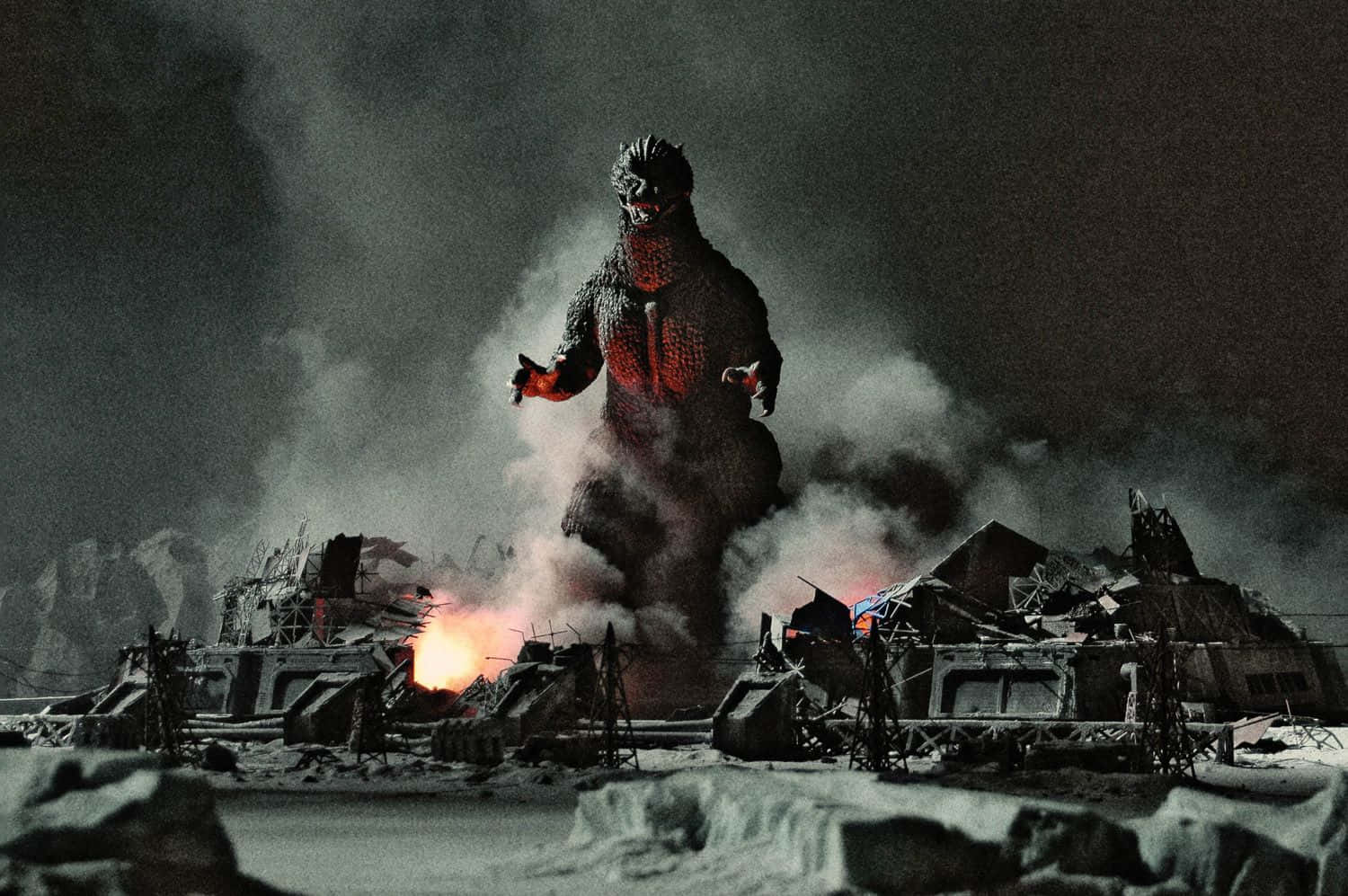 Classic Godzilla 桌布 壁紙 — 高聳的哥斯拉站在白雪覆蓋的廢墟中，熾熱的爆炸照亮了黑暗的夜空。