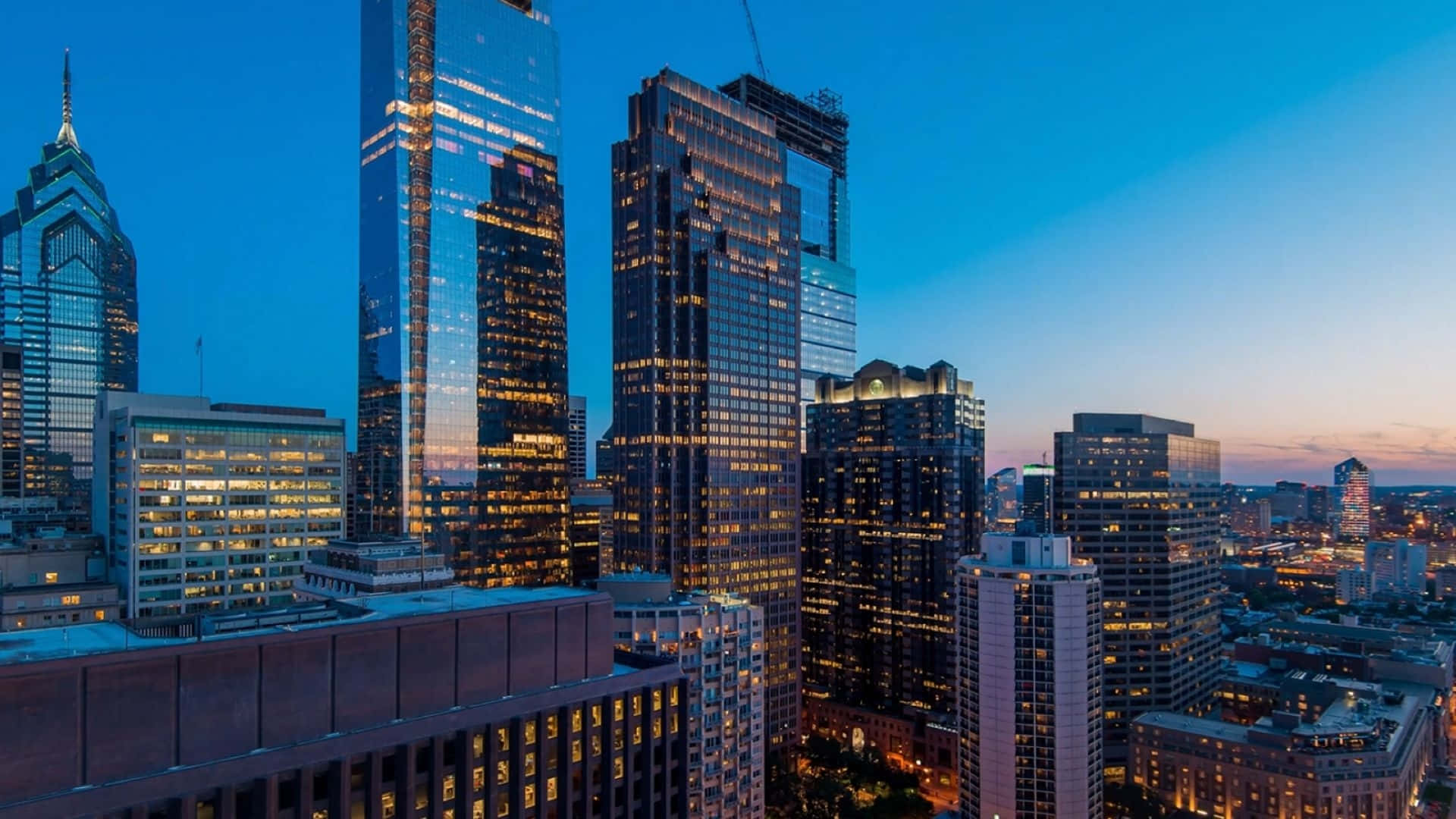 Buildings 桌布 壁紙 — 高聳的摩天大樓在暮色天空中散發溫暖的光芒，構成繁華的城市天際線。