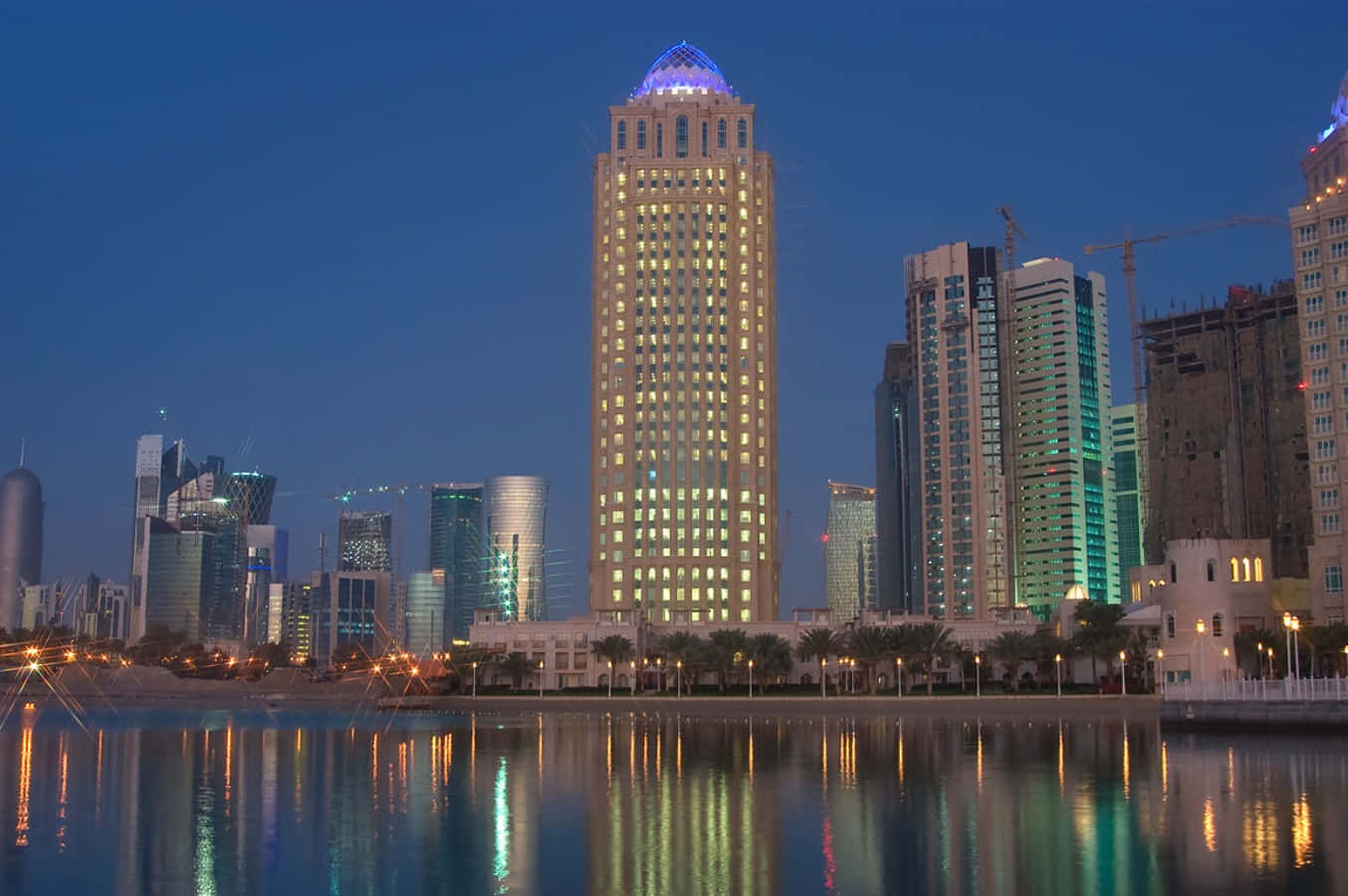Qatar 桌布 壁紙 — 高聳的摩天大樓閃爍著窗戶的光芒，在暮色天空下平靜的水面上倒映。