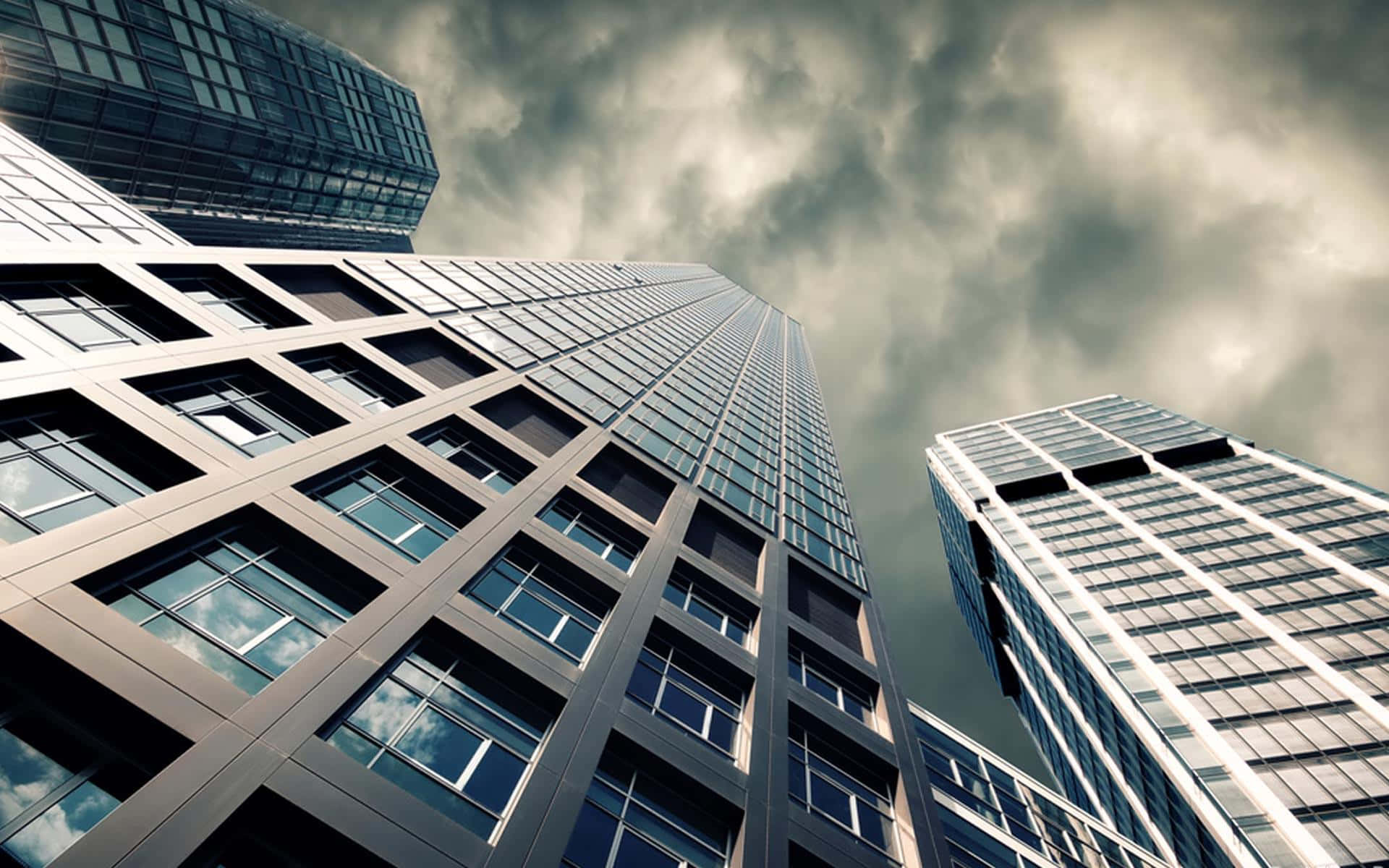 Buildings 桌布 壁紙 — 高聳的玻璃摩天大樓在低角度城市拍攝中刺穿戲劇性的多雲天空。