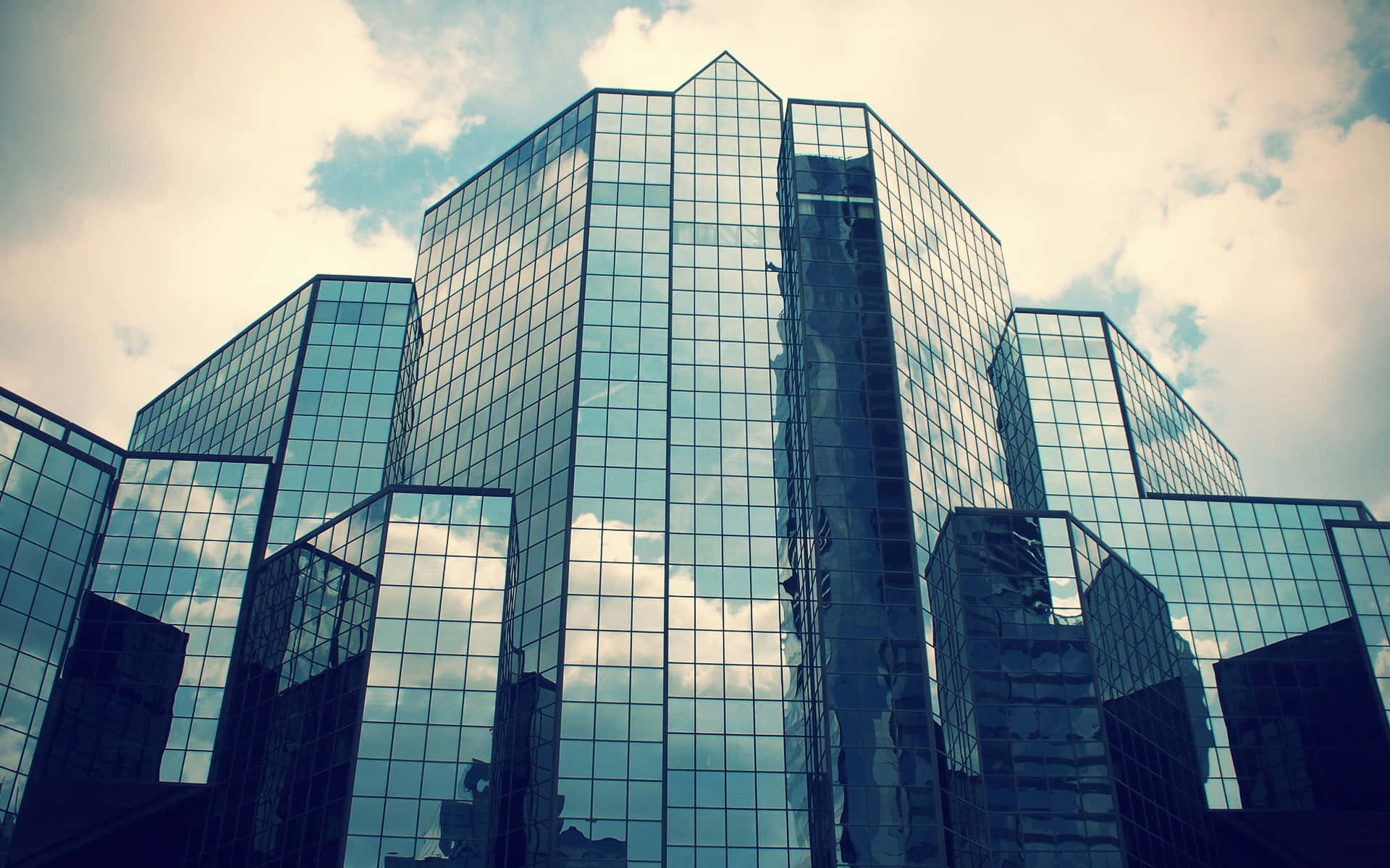 Buildings 桌布 壁紙 — 高聳的玻璃摩天大樓在戲劇性的低角度城市拍攝中反射多雲的天空。