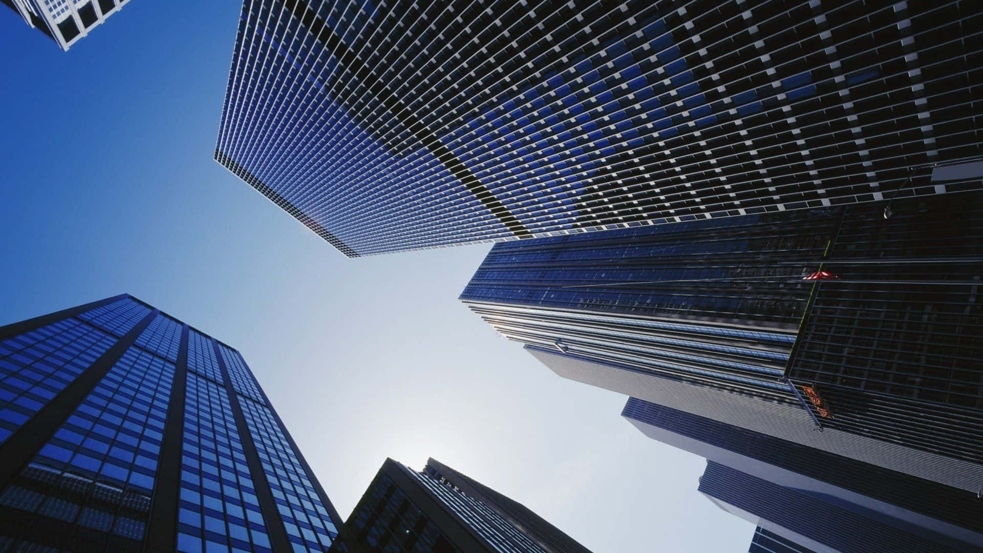 Buildings 桌布 壁紙 — 高聳的玻璃摩天大樓在戲劇性的低角度城市鏡頭中刺穿清澈的藍天。