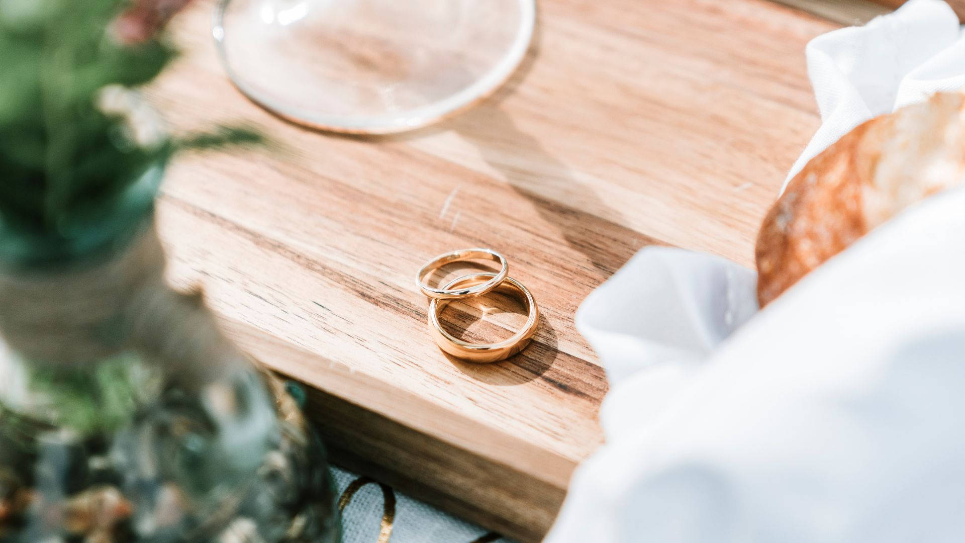 木托盤上的兩枚金結婚戒指，附玻璃杯和白色布。