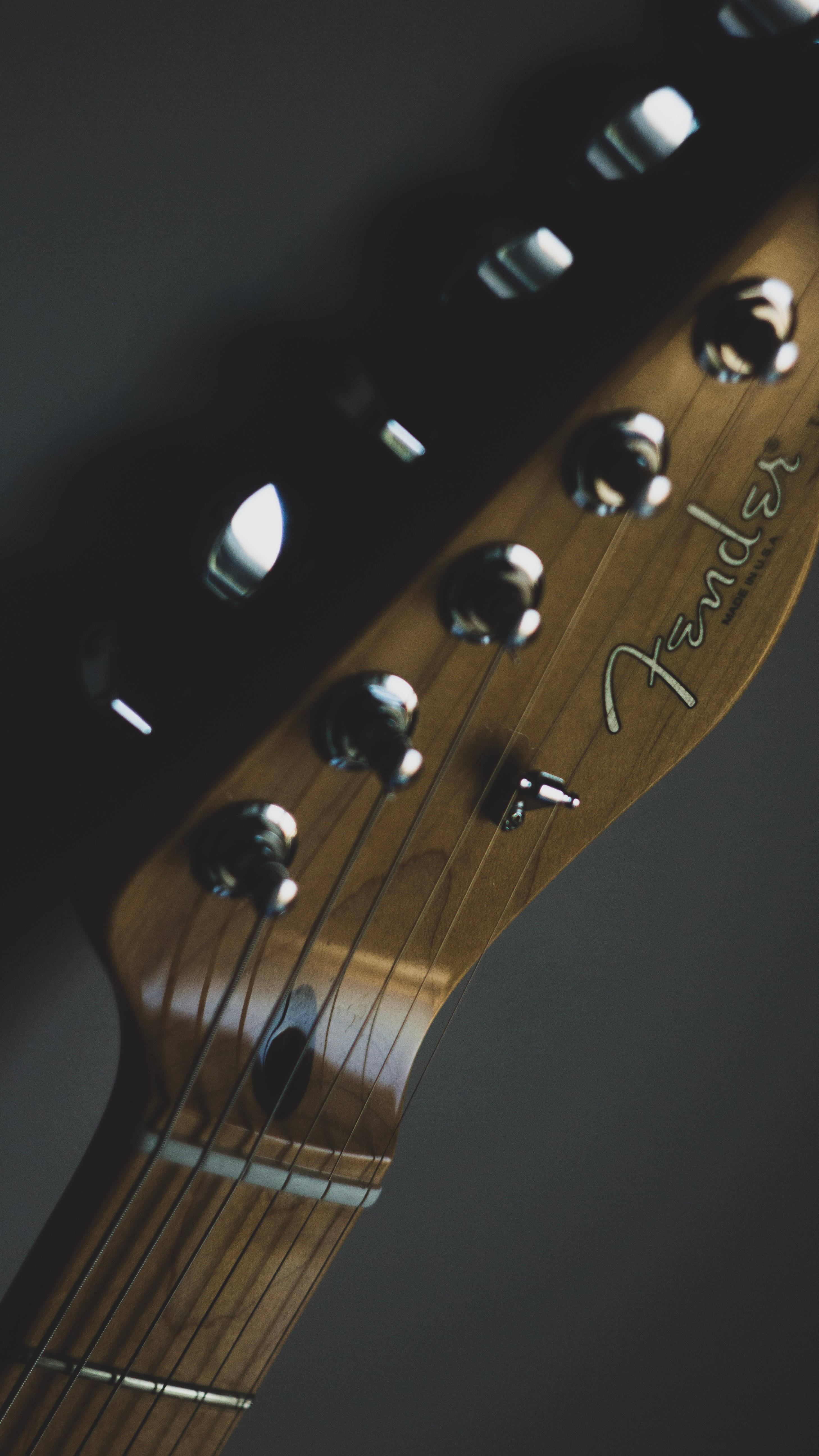 高解析度 iPhone 吉他 壁紙 — Fender 結他頭部特寫，帶有鉻合金調音栓和木紋，在柔和燈光下。