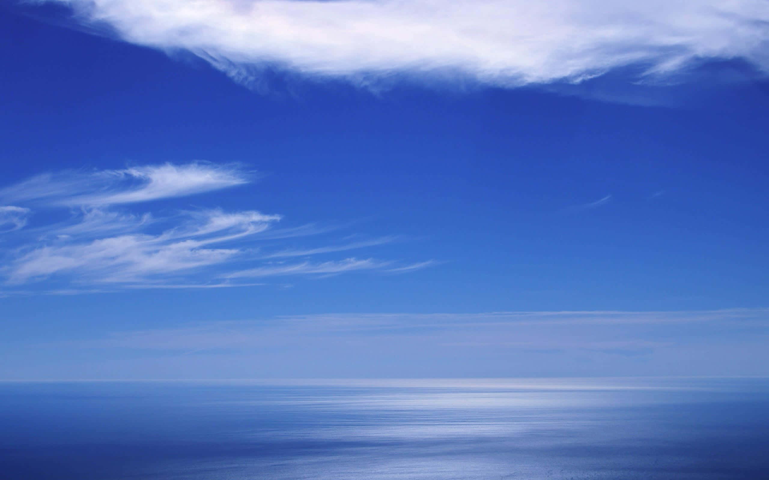 高解析度天空與蔚藍海洋 壁紙 — 廣闊平靜的海洋在柔和縷縷雲彩下，以寧靜的藍色調與無盡的天空相遇。
