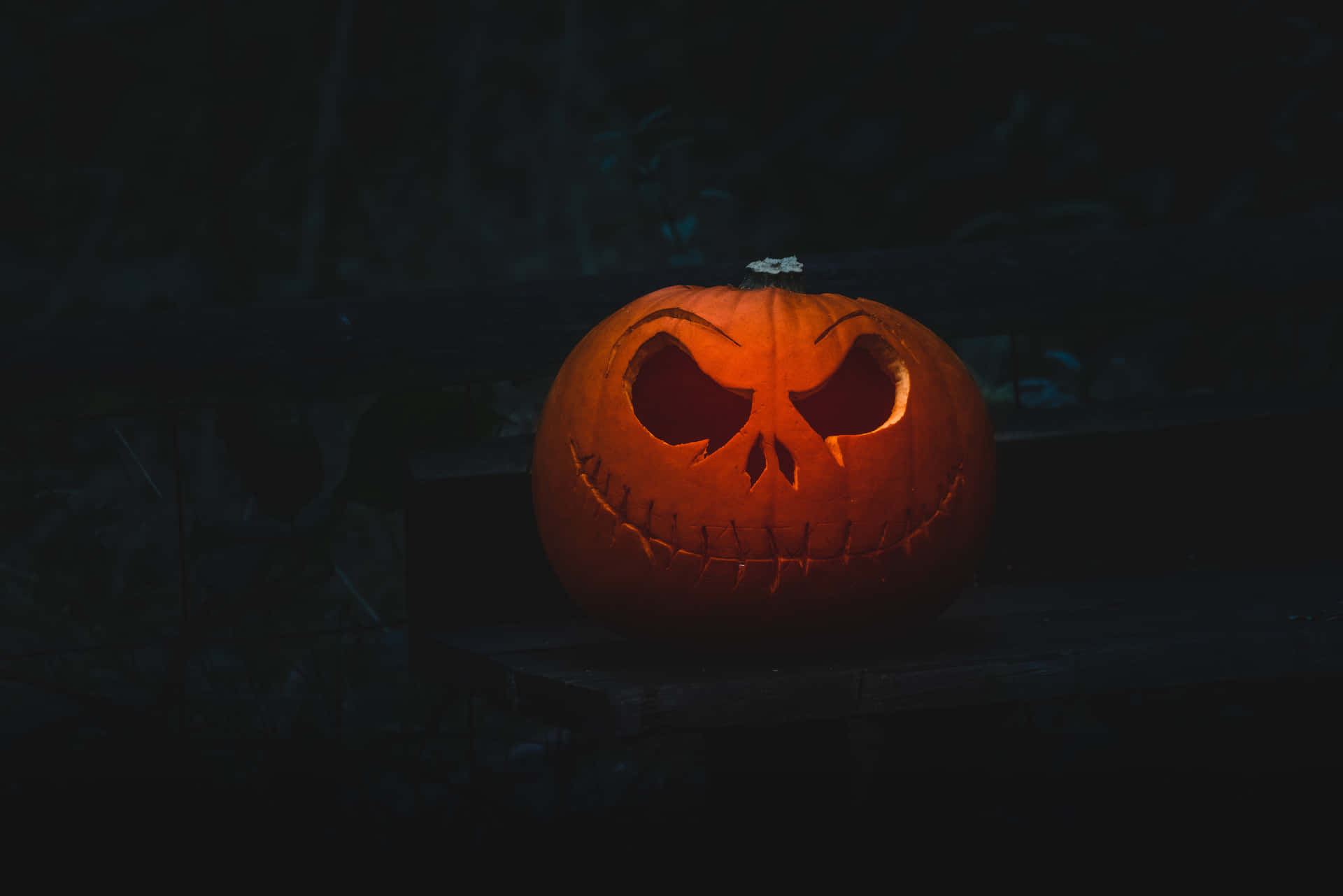 夜間木長椅上帶縫合嘴巴的發光雕刻南瓜。