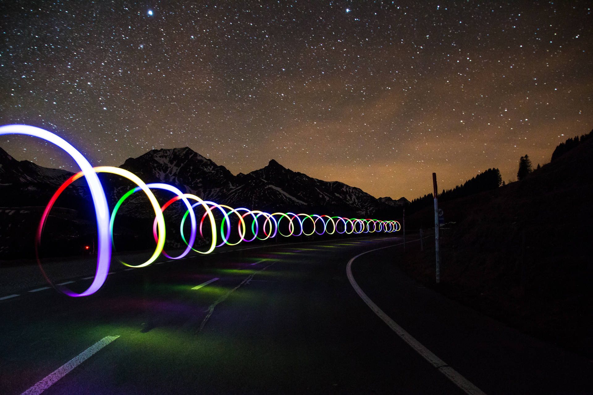 色彩繽紛的光圈沿著山路在繁星點點的夜空下延伸。