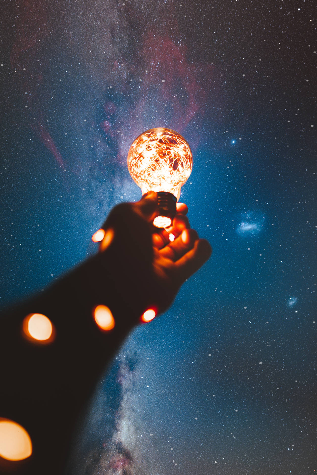 手在銀河下的星空夜空中拿著發光的燈泡