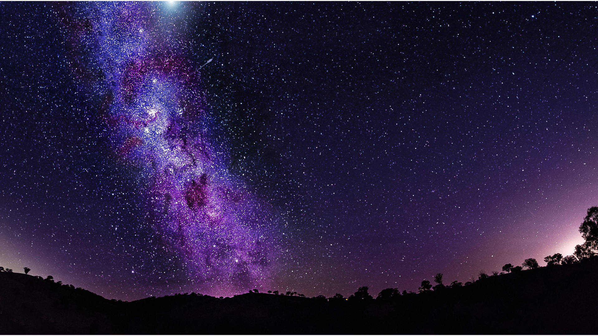 充滿活力的紫色和藍色星系在繁星點點的夜空下，在黑暗的山丘上拱起。