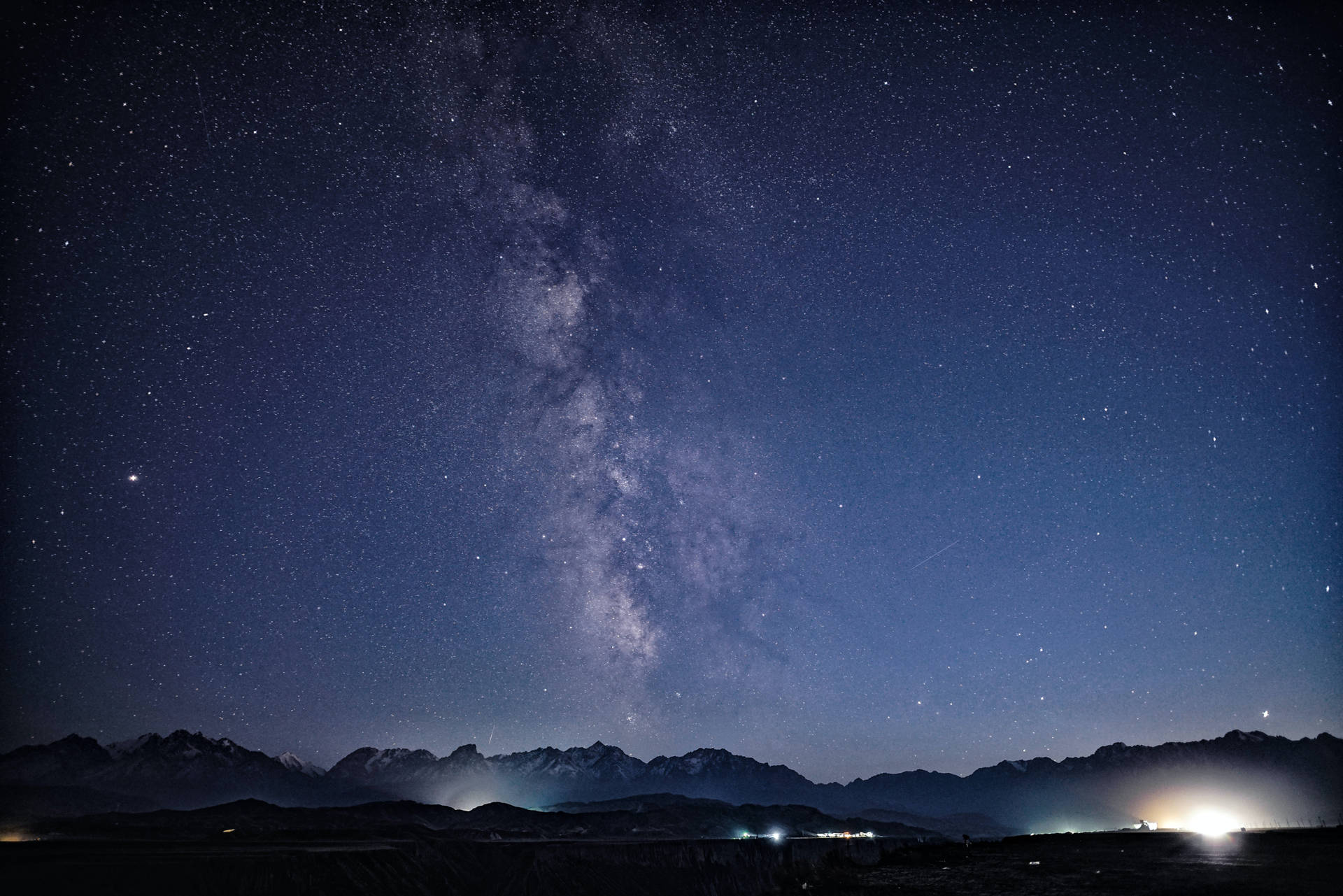 夜間積雪山峰上的銀河系與遠處燈光。
