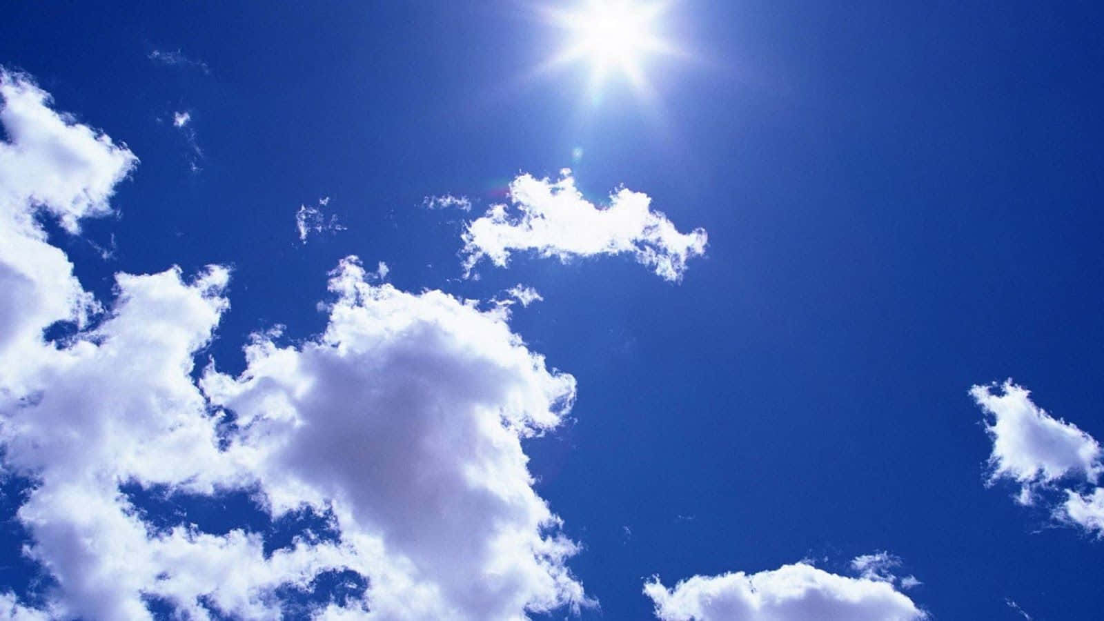 高解析度晴空與太陽 壁紙 — 燦爛的太陽在鮮豔的藍天中透過蓬鬆的白雲散發出明亮的光芒。