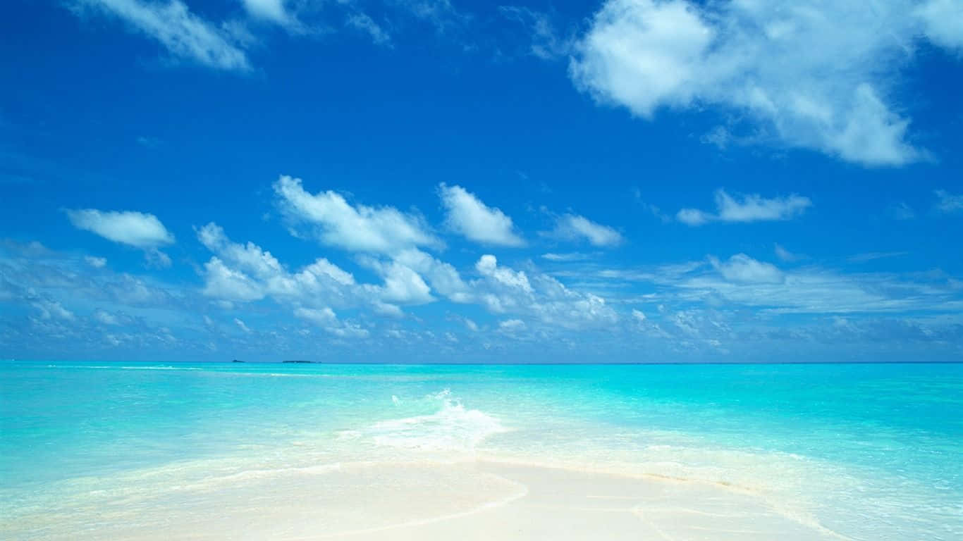 高解析度海邊天空 壁紙 — 純淨的白色沙灘與碧綠的海水相遇，在點綴著蓬鬆白雲的湛藍天空下。